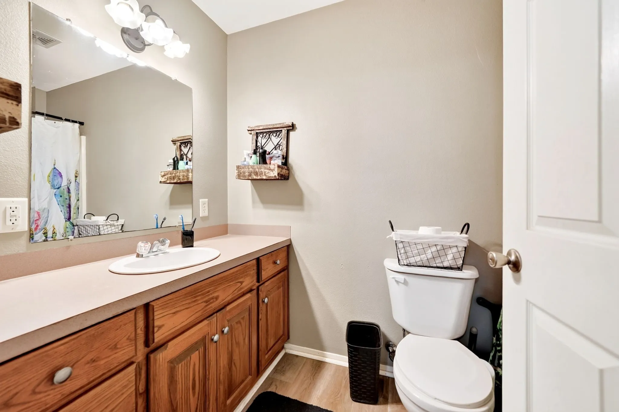 Bathroom featuring an extended vanity with wood-finish cabinetry and an integrated sink, a large wall-mounted mirror, and wood-finish flooring