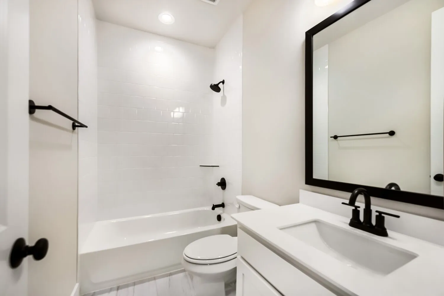 Bathroom featuring a bathtub with subway tile surround, matte black fixtures, a single-sink vanity with white countertop, and recessed lighting