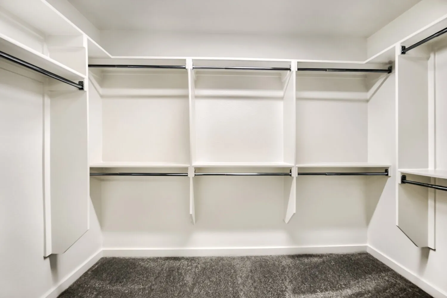 Custom built-in white shelving, multiple hanging rods, and gray carpeted flooring
