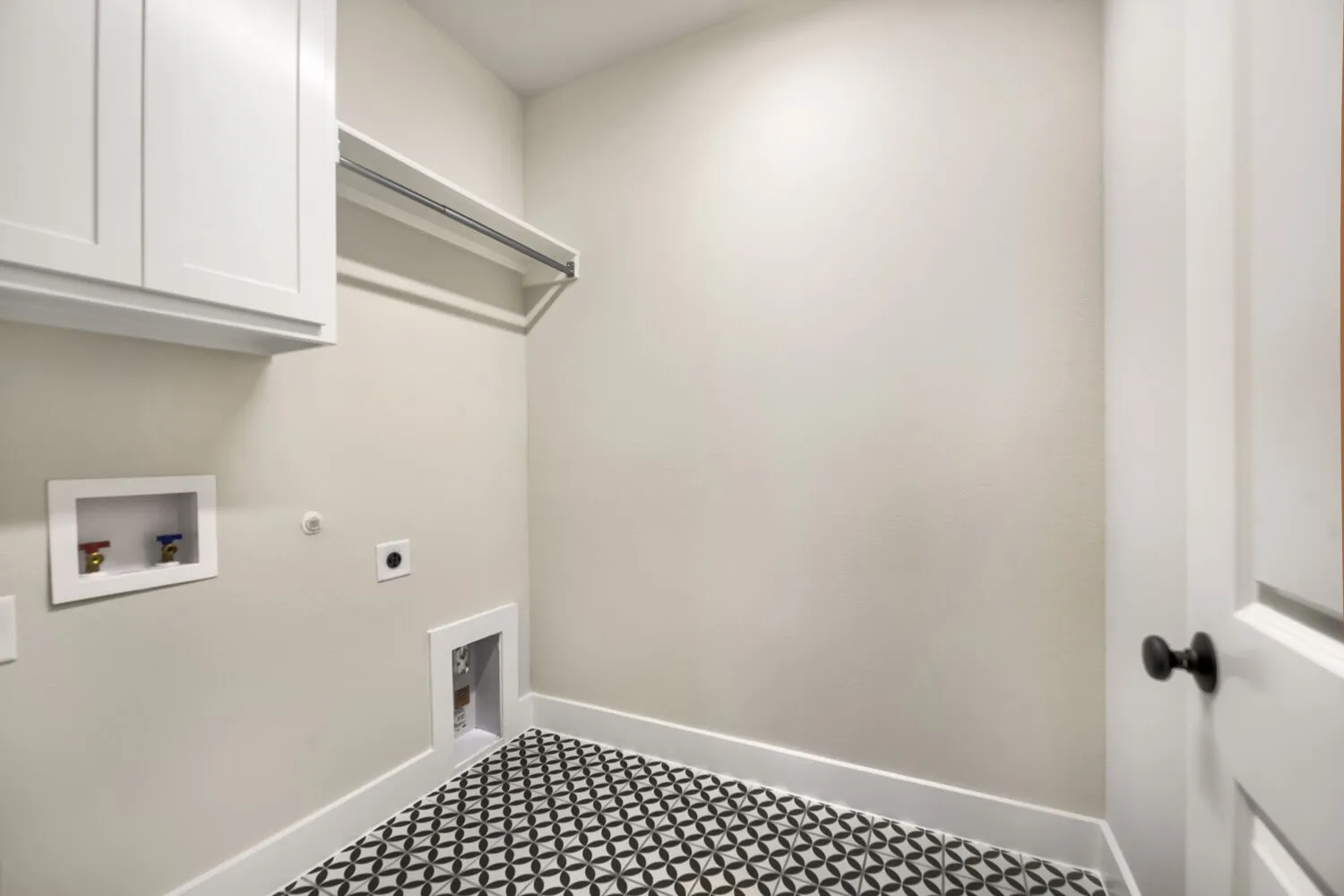 Laundry area featuring white cabinetry, a hanging rod, light neutral wall paint, and geometric pattern tile flooring