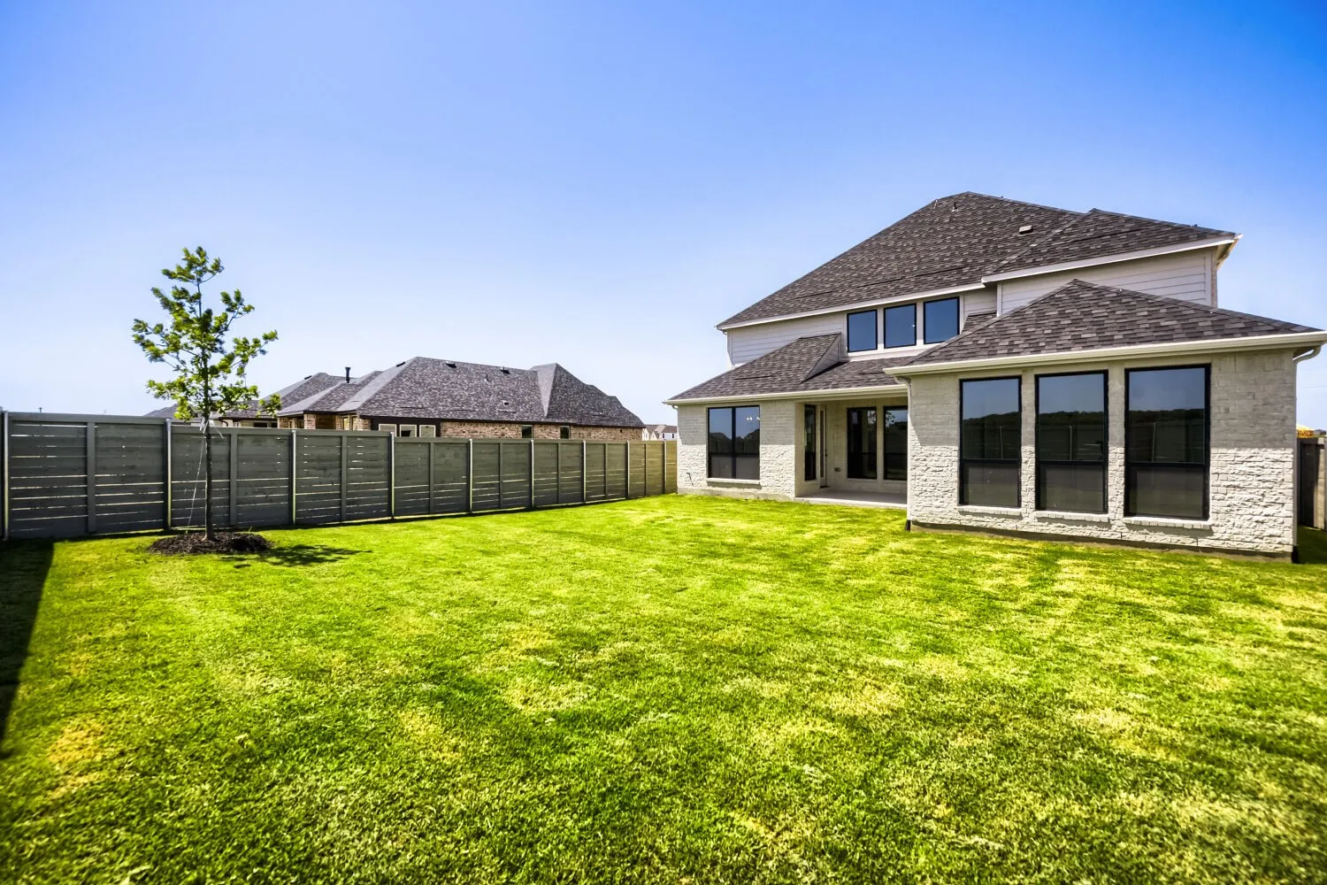 Expansive backyard with a manicured lawn, full perimeter fencing, and a newly constructed residential structure with multiple windows