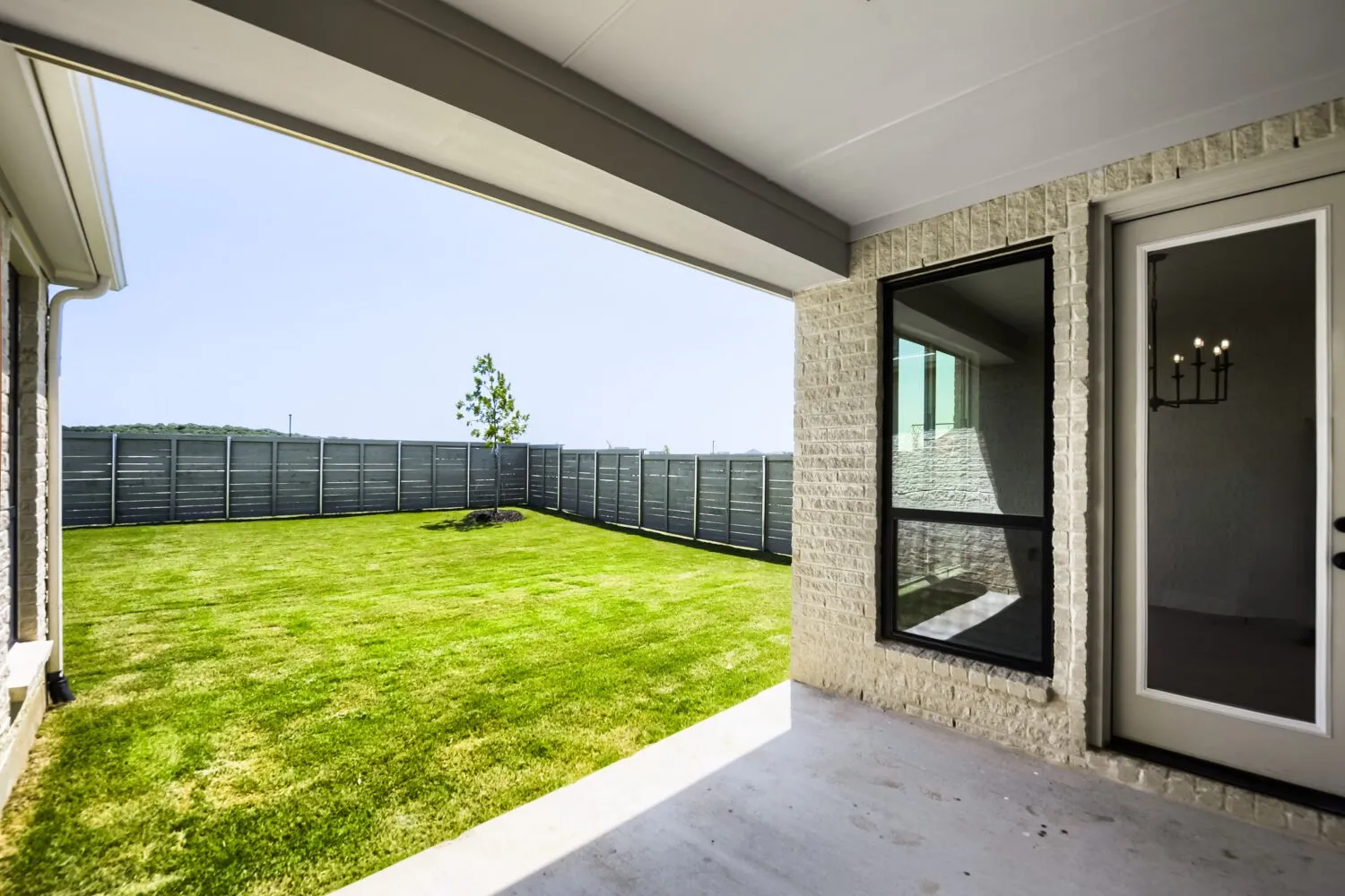 Covered patio with concrete flooring, light-colored brick exterior, and a full-light glass door