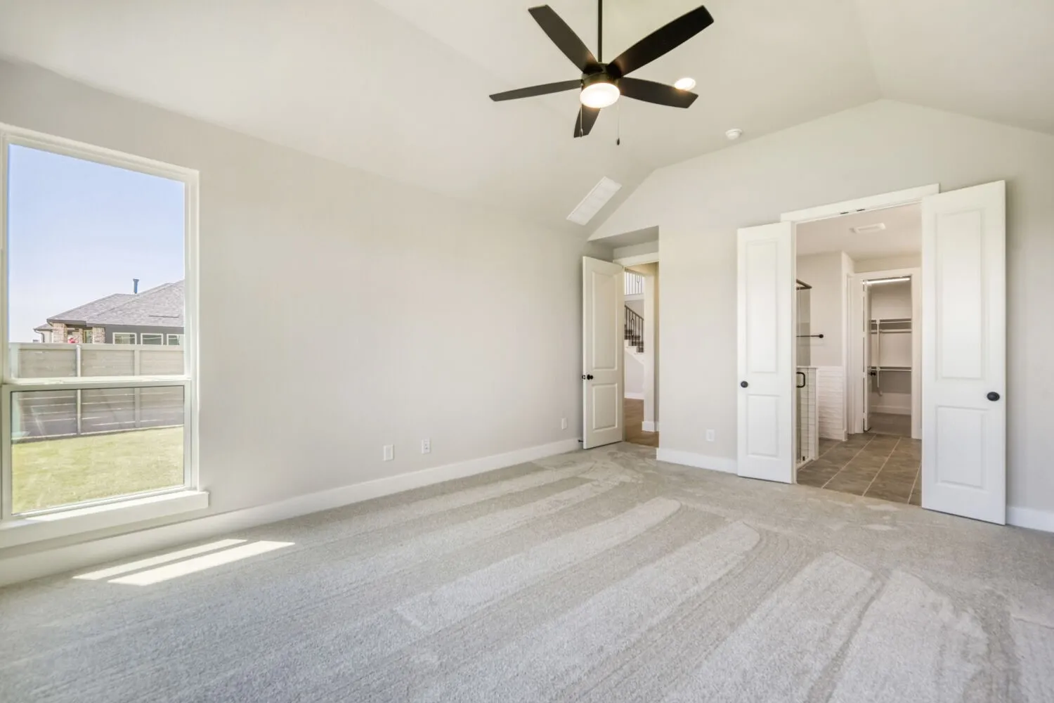 Vaulted ceiling with an attached ceiling fan, large window, light gray carpeting, and white interior doors with dark hardware