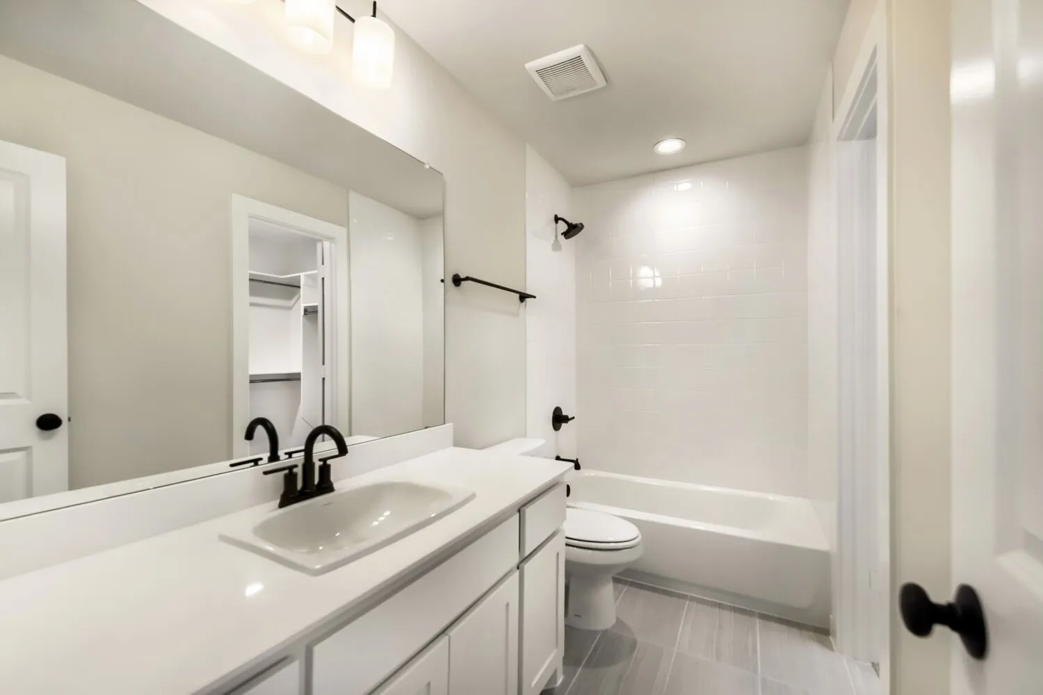 Modern bathroom featuring a rectangular vessel sink set atop a white vanity with ample countertop space, polished chrome faucet and hardware, large framed mirror, ceramic tile flooring, and an alcove bathtub with glass enclosure and matte black fixtures