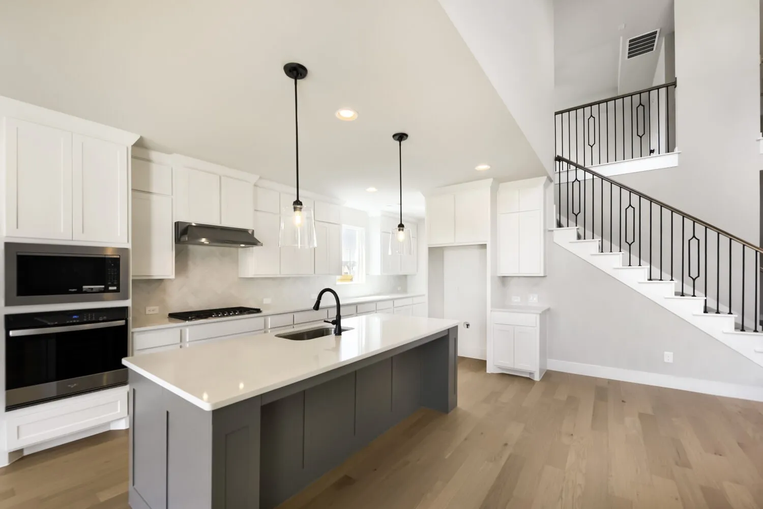 Kitchen featuring white shaker cabinetry, stainless steel appliances, a center island with pendant lighting, and wood-finish flooring