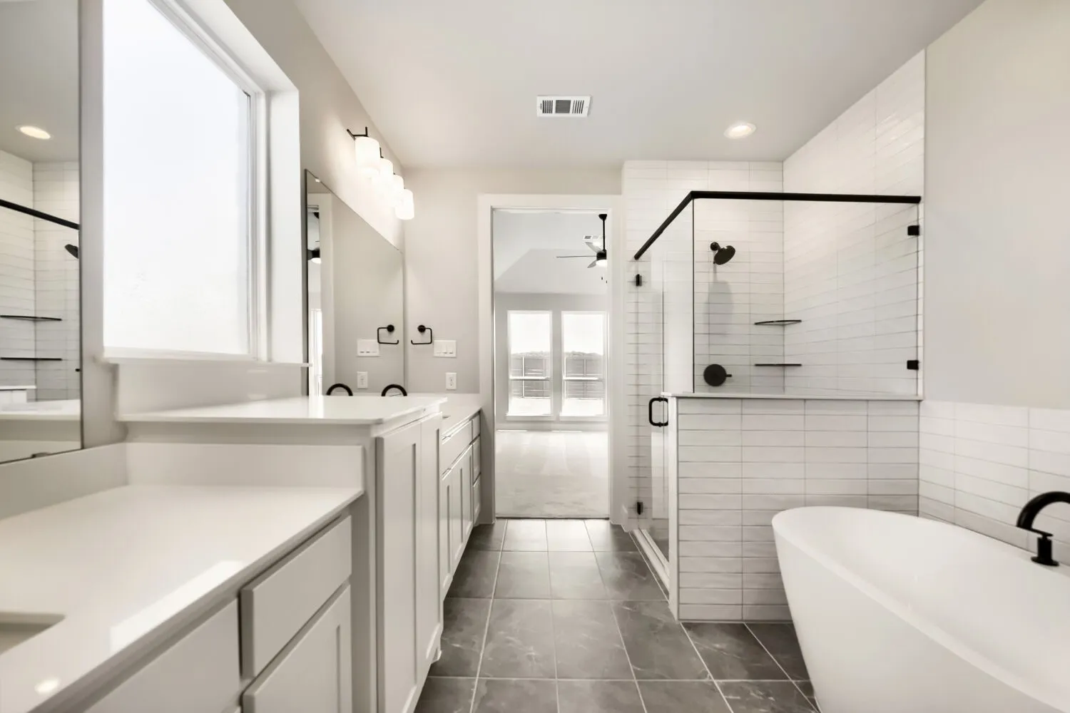 Dual sink vanity with white countertops, walk-in shower with black-framed glass enclosure, freestanding bathtub, and tiled flooring