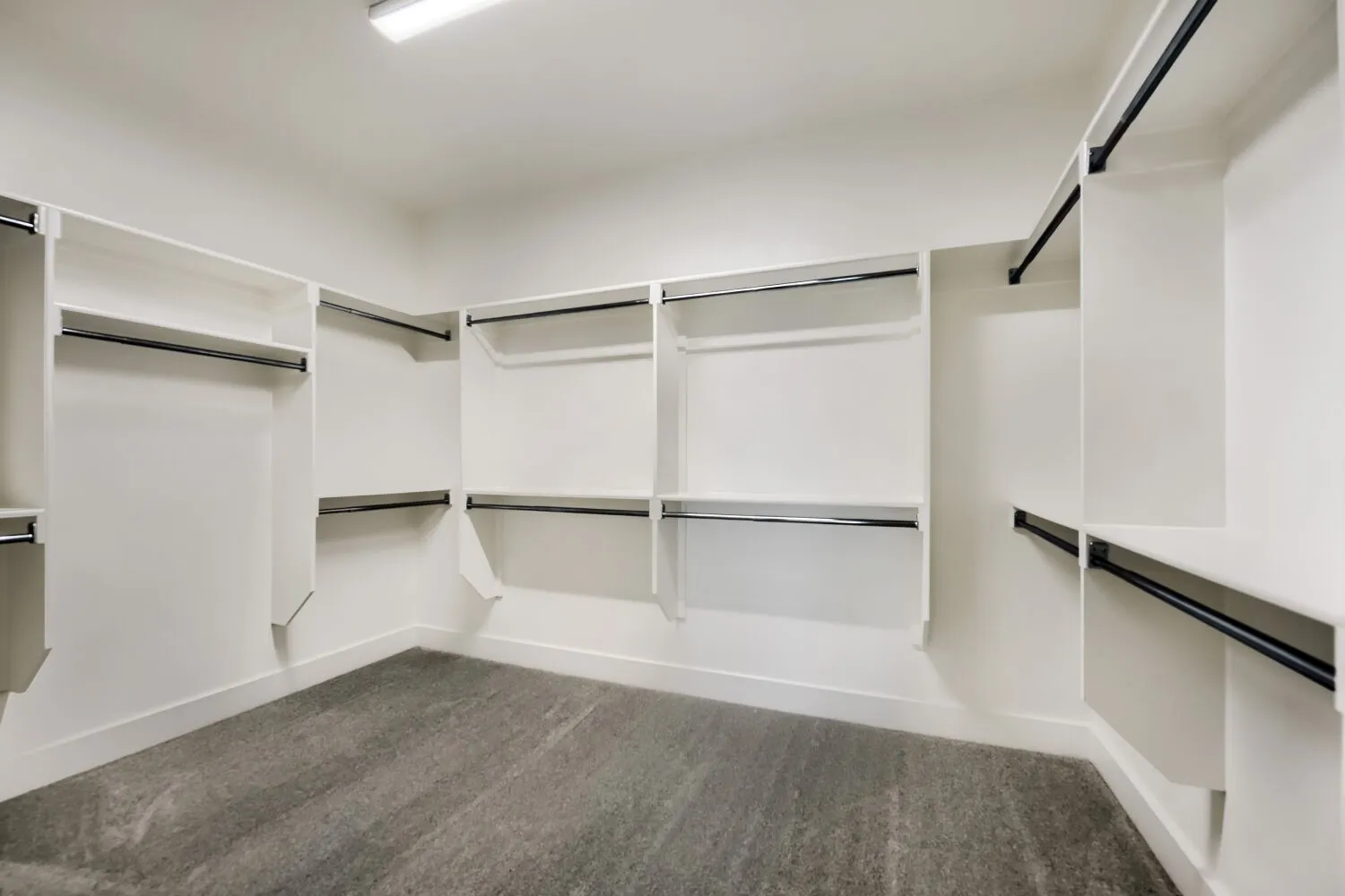 Custom closet organization system featuring multiple hanging rods and shelving, enhanced by overhead flush-mount lighting and plush carpeting