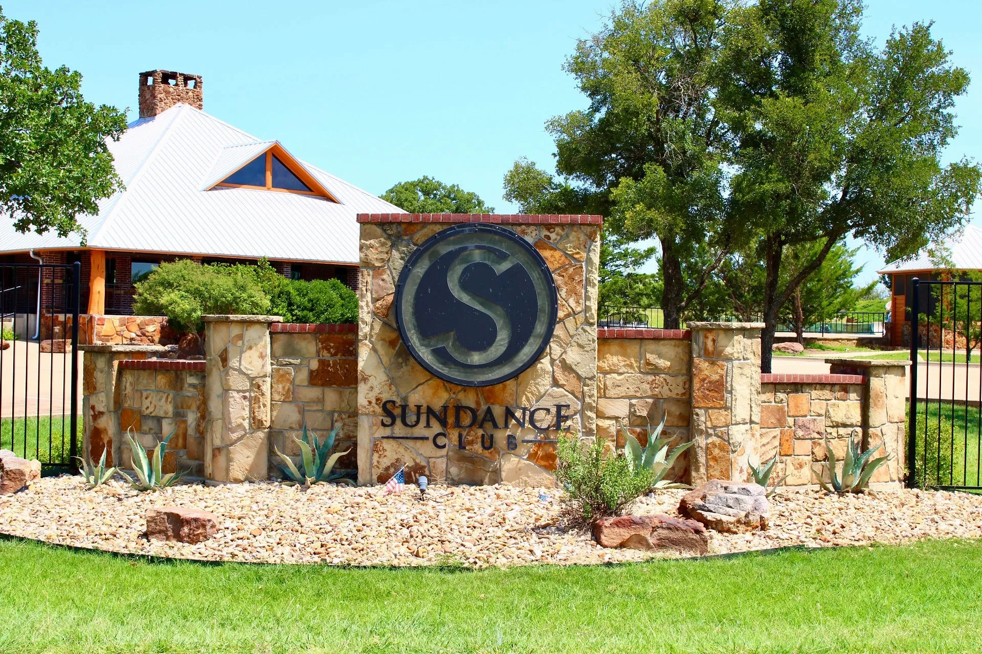 Stone and brick entry monument with iron fencing, gravel landscaping, and established plantings