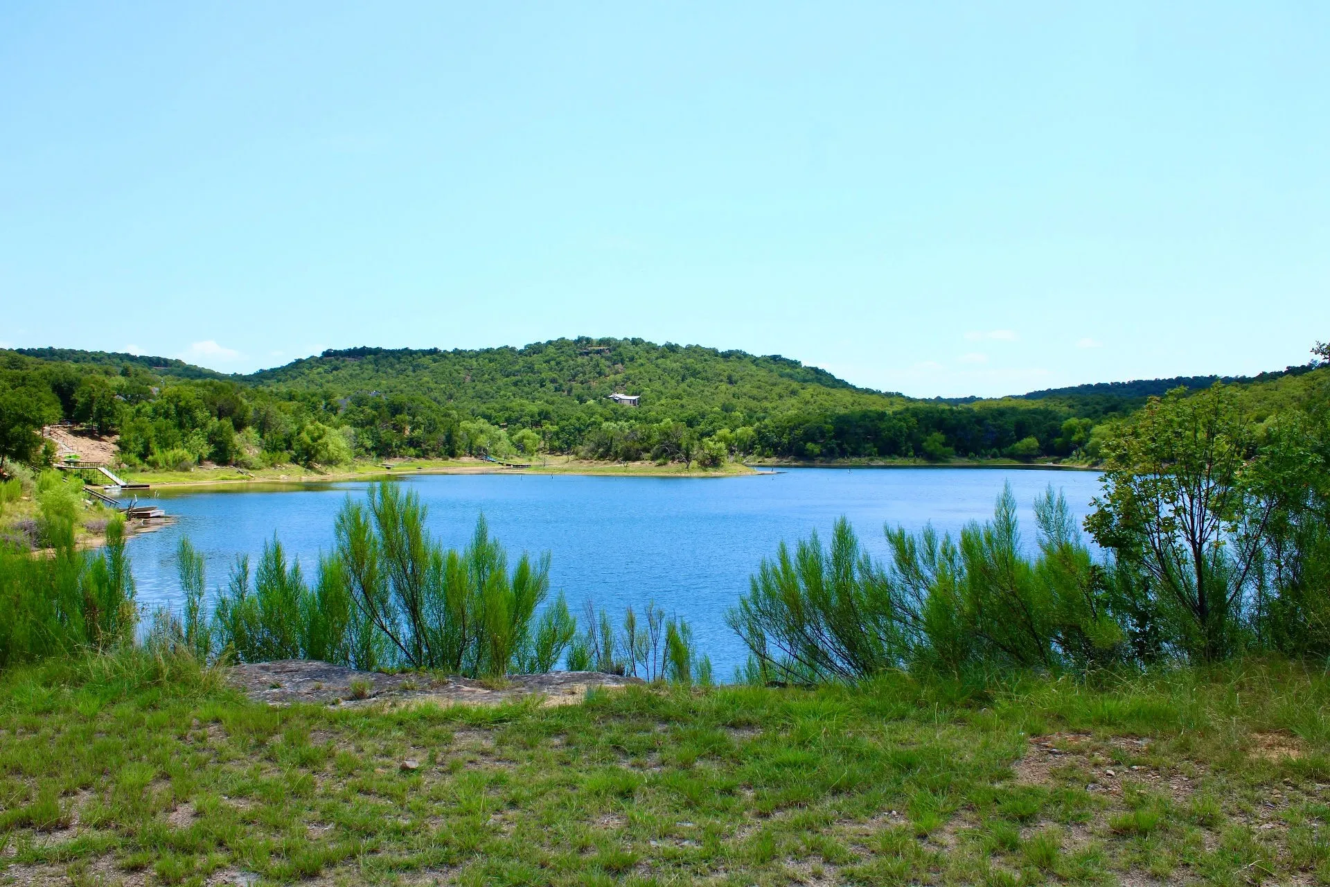 Expansive water frontage featuring a blue lake, a wooded shoreline, rolling hills, and a clear blue​​‌​​​​‌​​‌‌​‌‌​​​‌‌​‌​‌​‌​​​‌​​ sky
