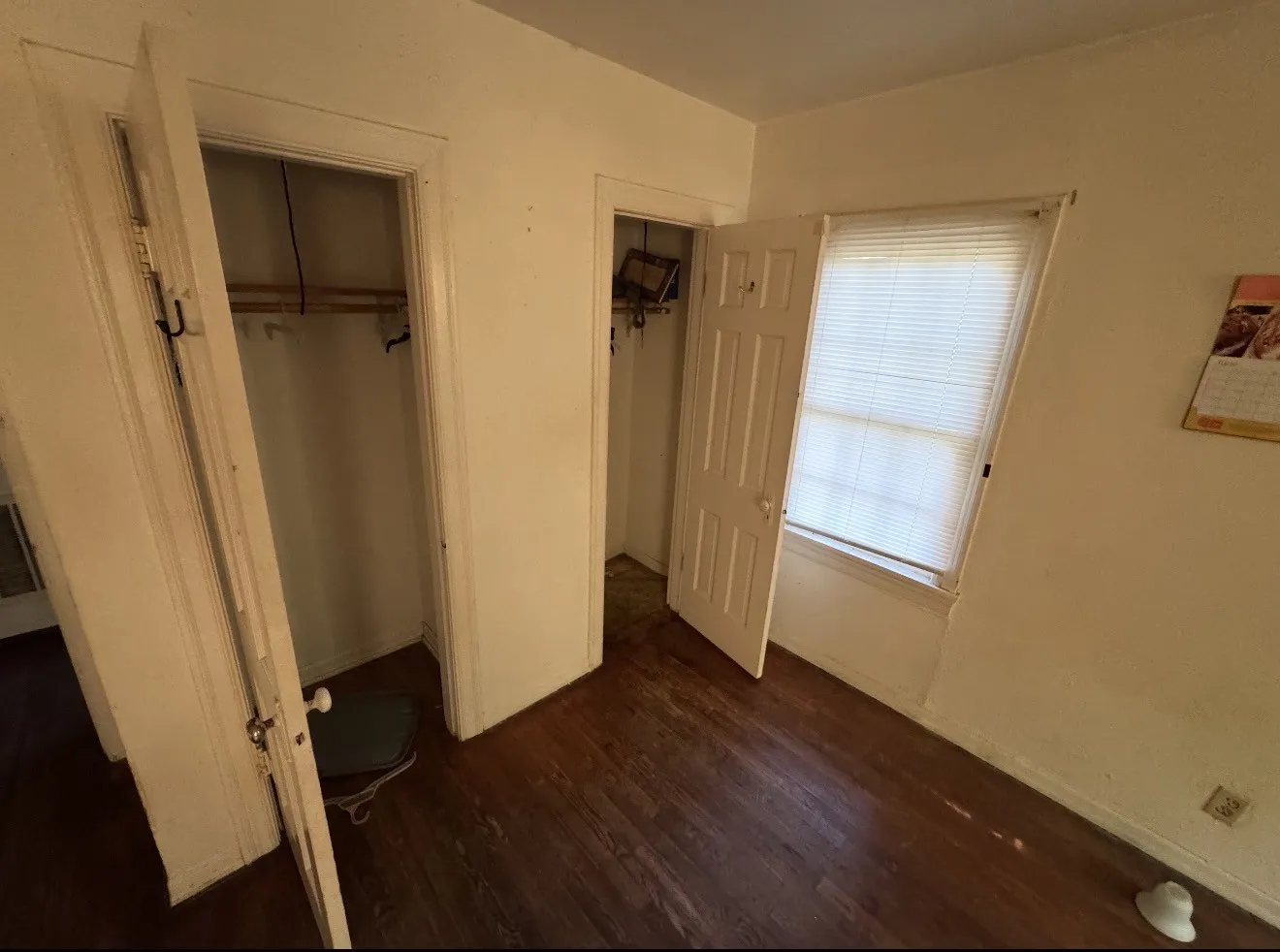 Room featuring wood-finish flooring, two closet entries, and a window with horizontal blinds