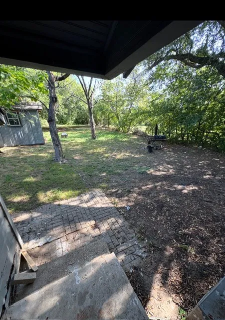 Expansive outdoor space featuring a paved patio area, mature trees, and a utility shed with corrugated siding