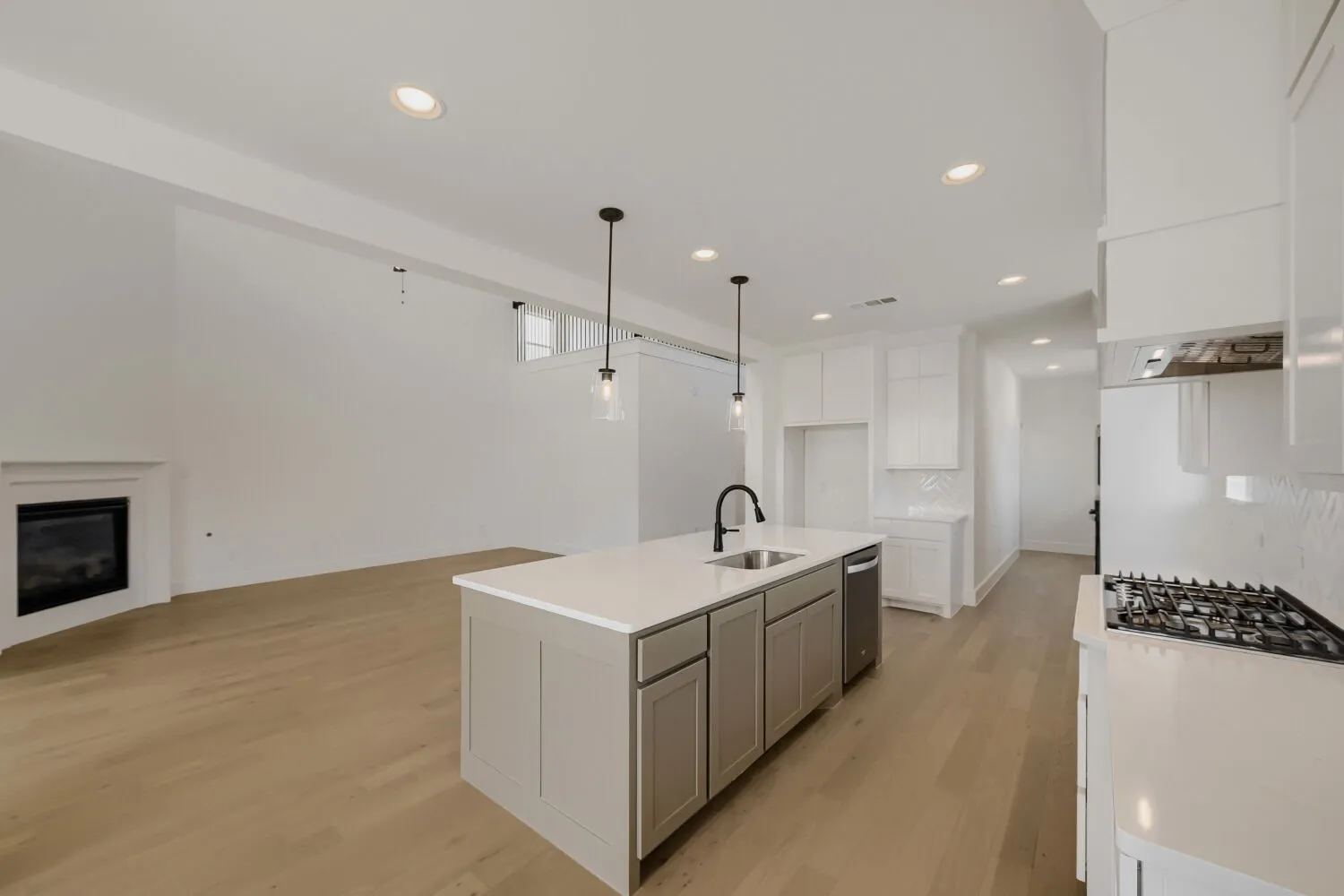 Kitchen island with a built-in sink and pendant lighting, gas range with hood, wood-finish flooring, and a corner fireplace
