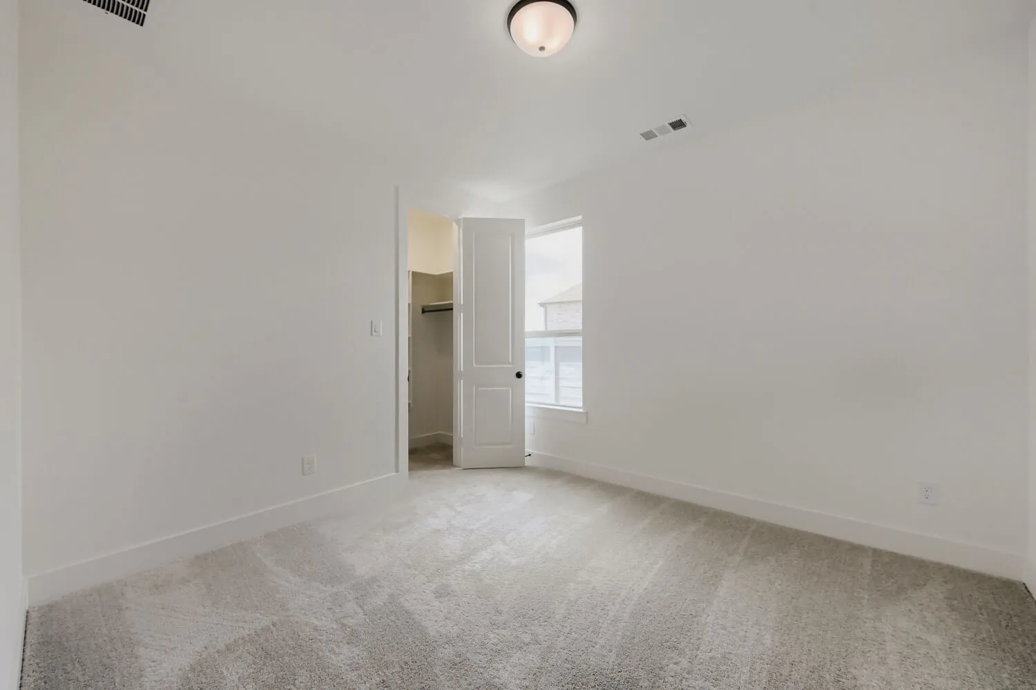 Neutral wall palette, ceiling-mounted light fixture, white interior door, window with natural light, and carpeted flooring