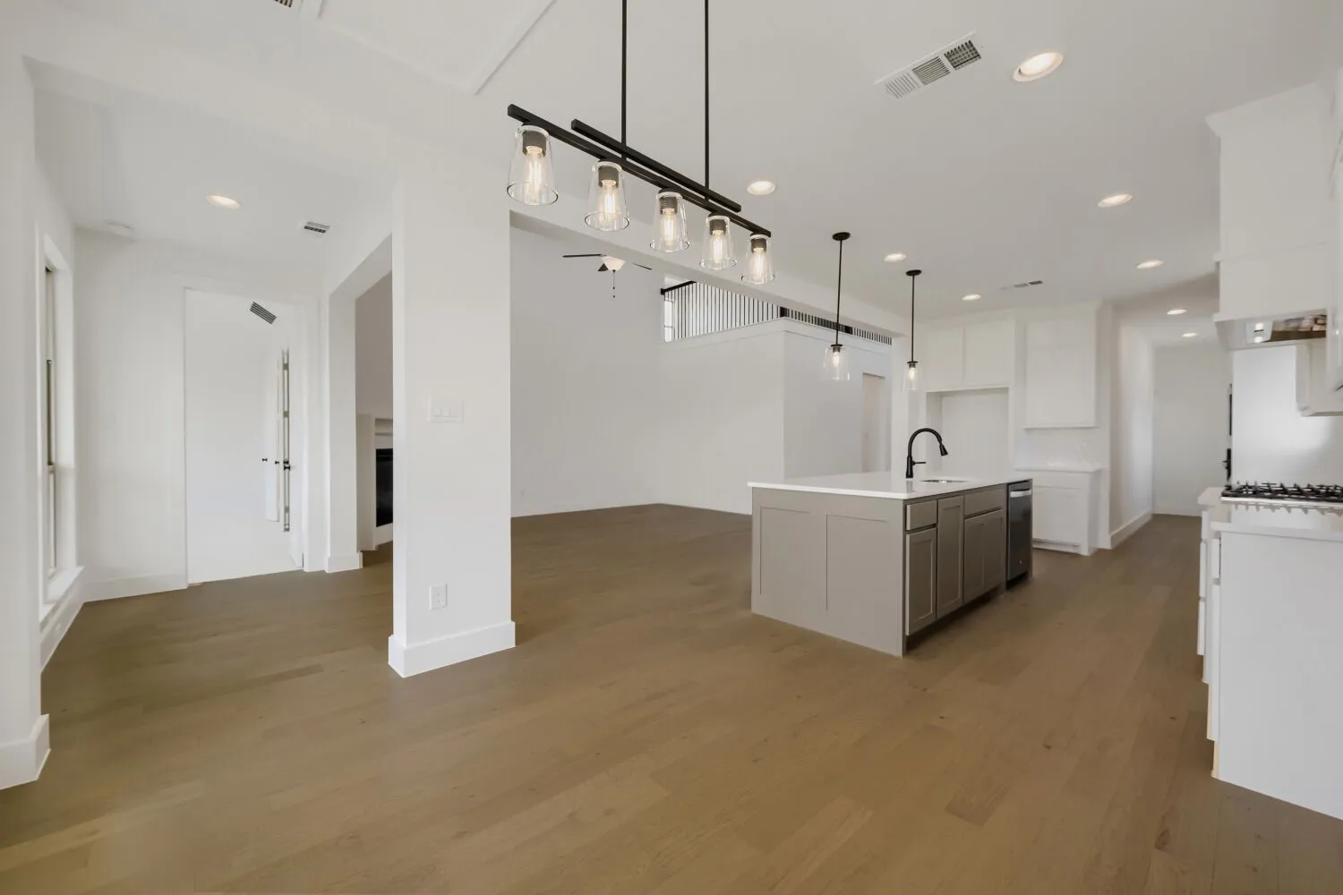 Open-concept living area with wood-finish flooring, recessed lighting, and a kitchen island featuring a sink with a matte black faucet