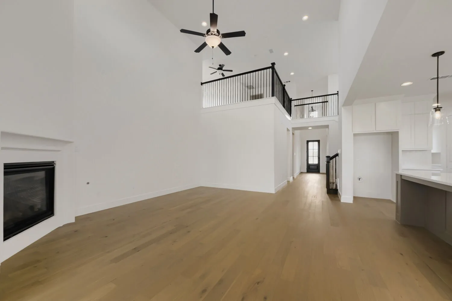 Vaulted ceilings with ceiling fans, wood-finish flooring, fireplace with white mantel, open concept design, and an upper-level railing