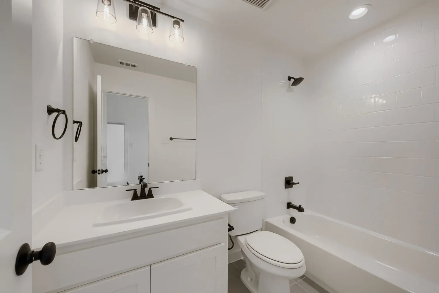 Vanity with an integrated sink and white countertop, black fixtures, framed mirror, and subway tile shower surround