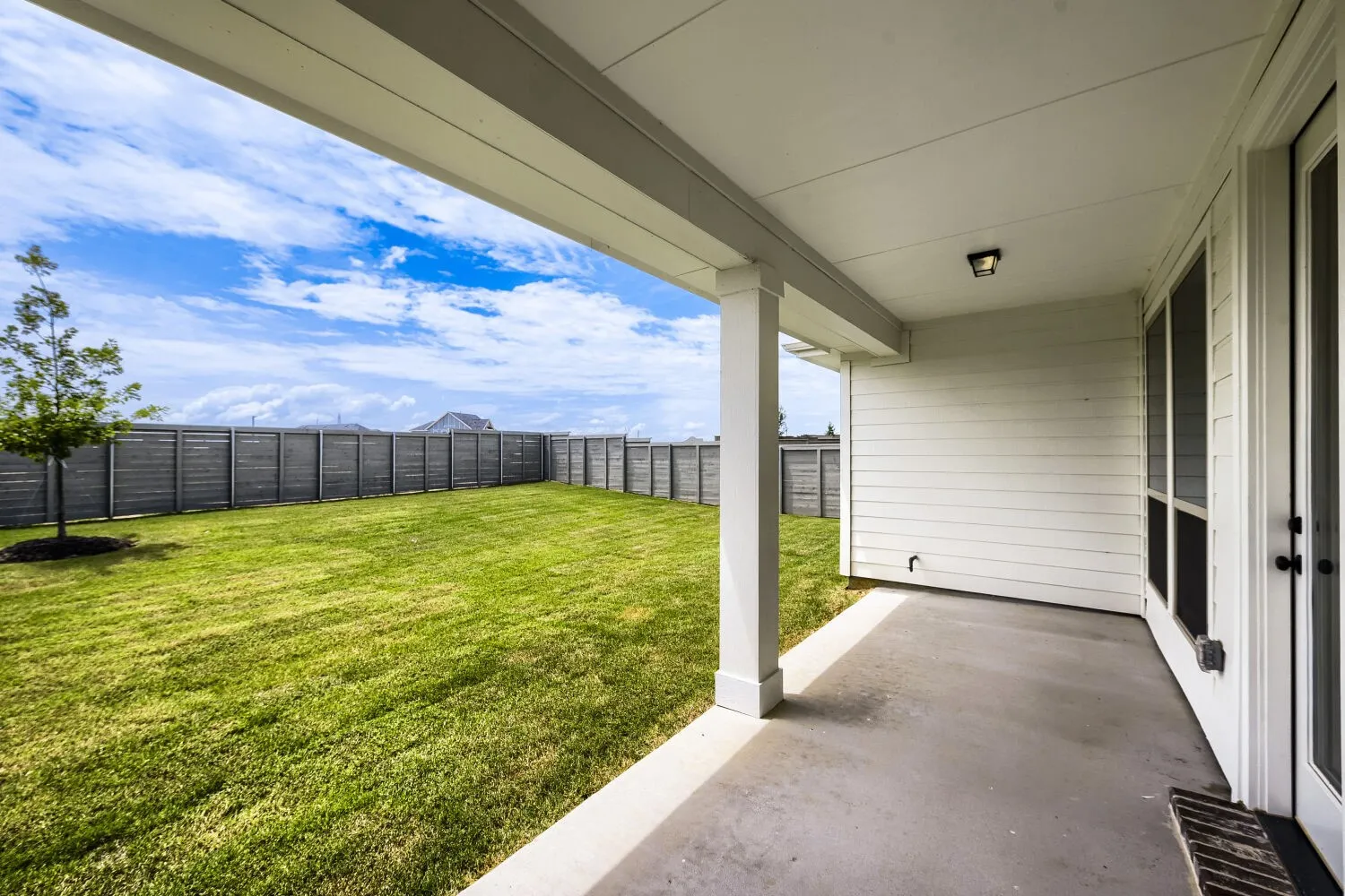 Expansive backyard with manicured lawn, full privacy fencing, and a covered concrete patio