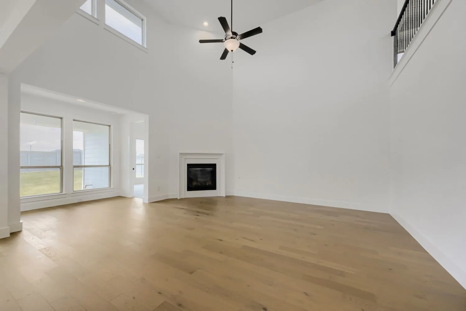 Vaulted ceiling with a ceiling fan, fireplace with a white mantel, wood-finish flooring, and multiple windows