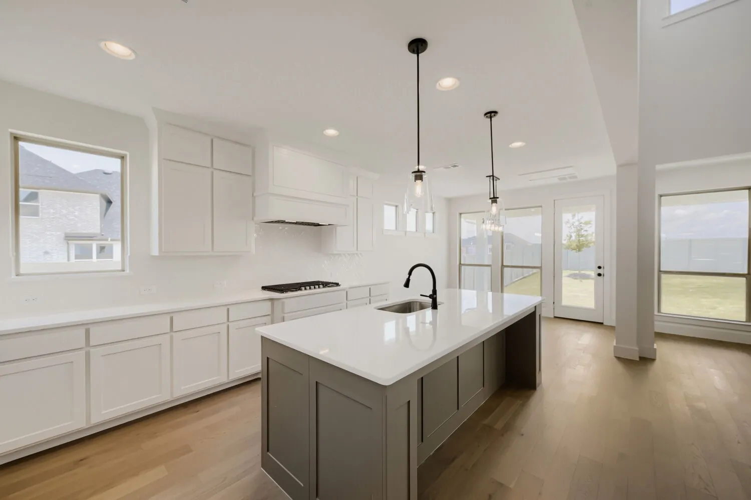 Kitchen featuring a large center island with a sink, white cabinetry, a gas range with a range hood, and wood-finish flooring