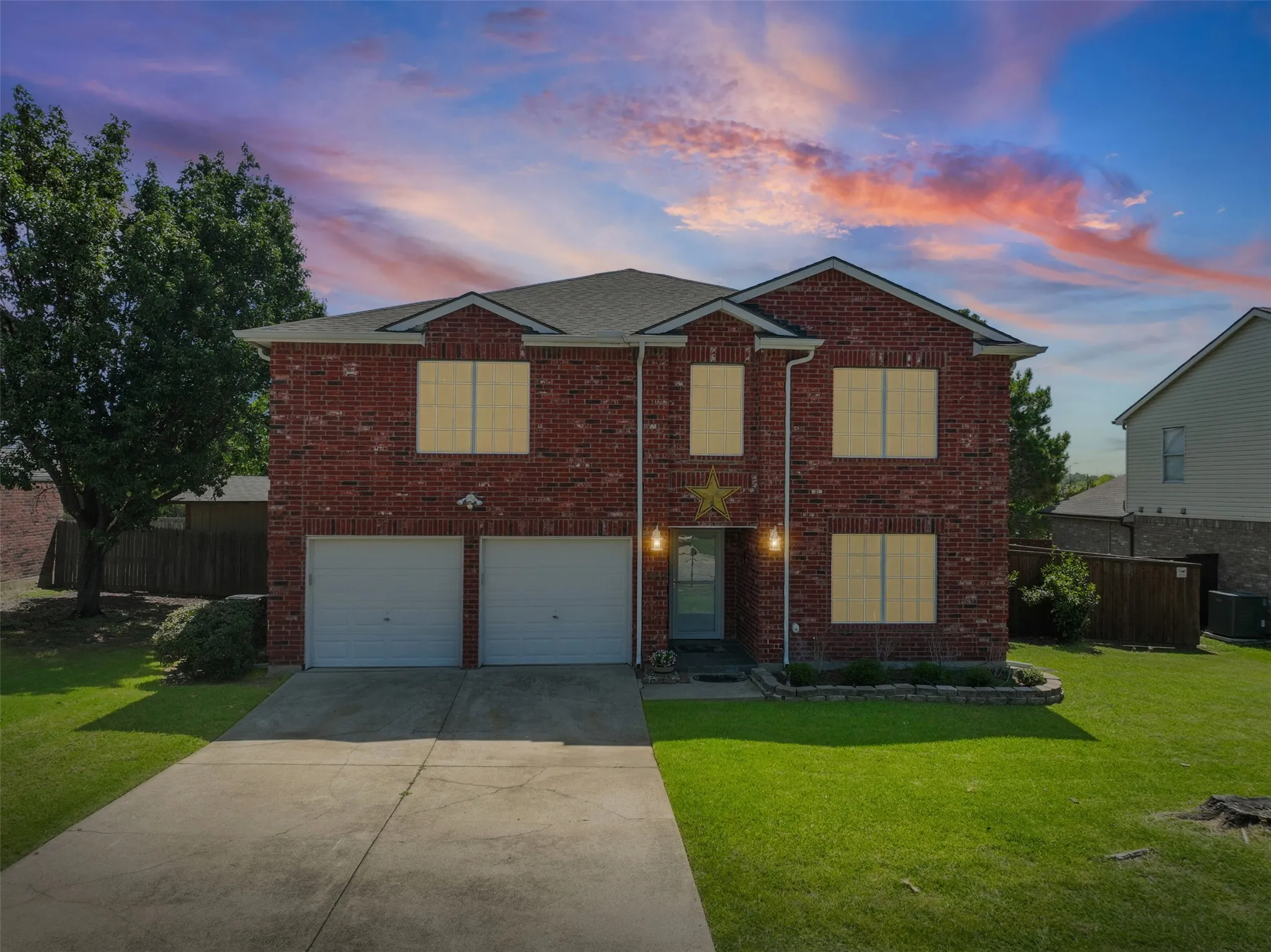 Two-story brick facade residence featuring a double-door garage, concrete driveway, and established front landscaping
