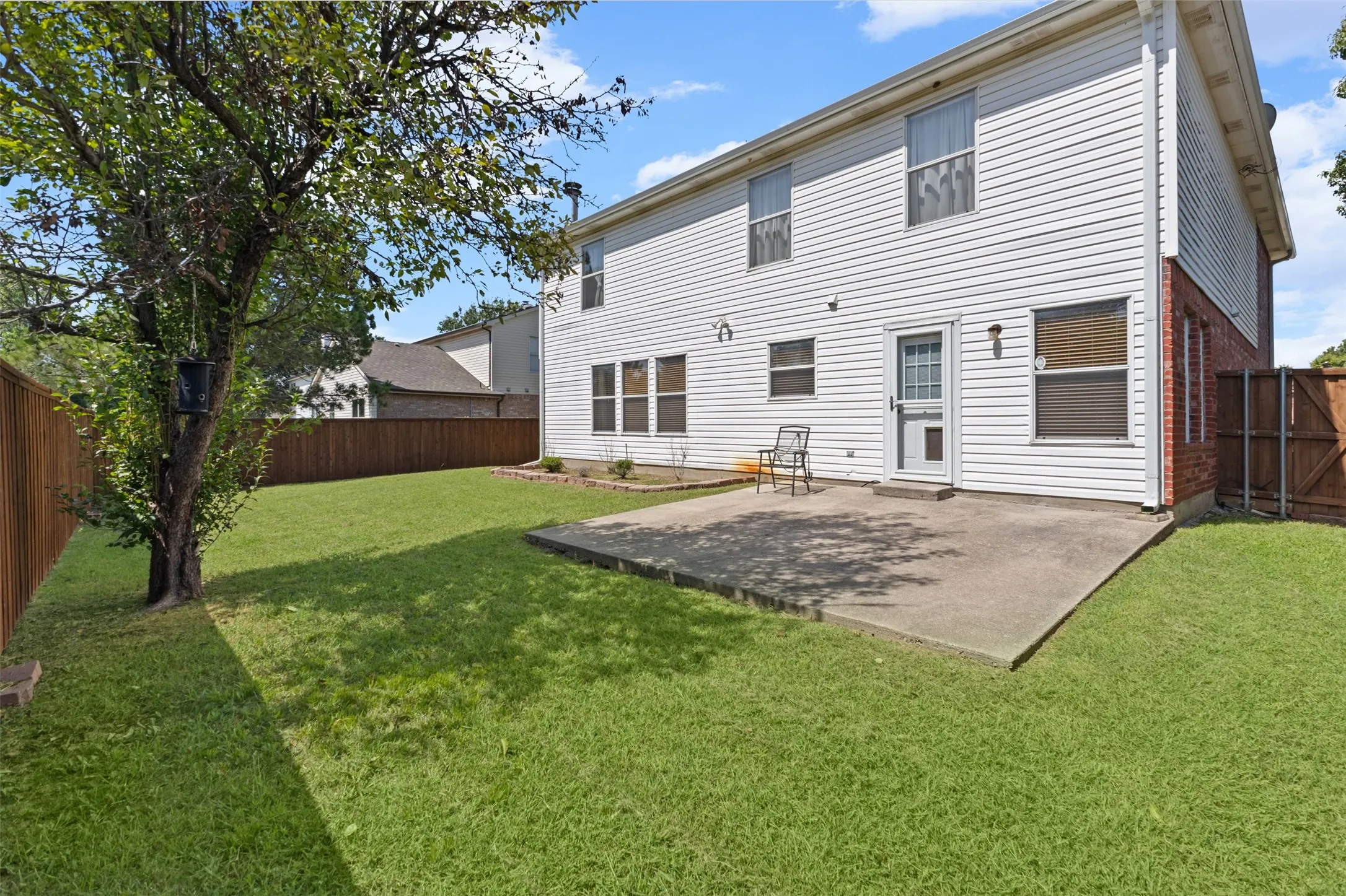 Expansive green lawn with a large shade tree, bordered by a privacy fence