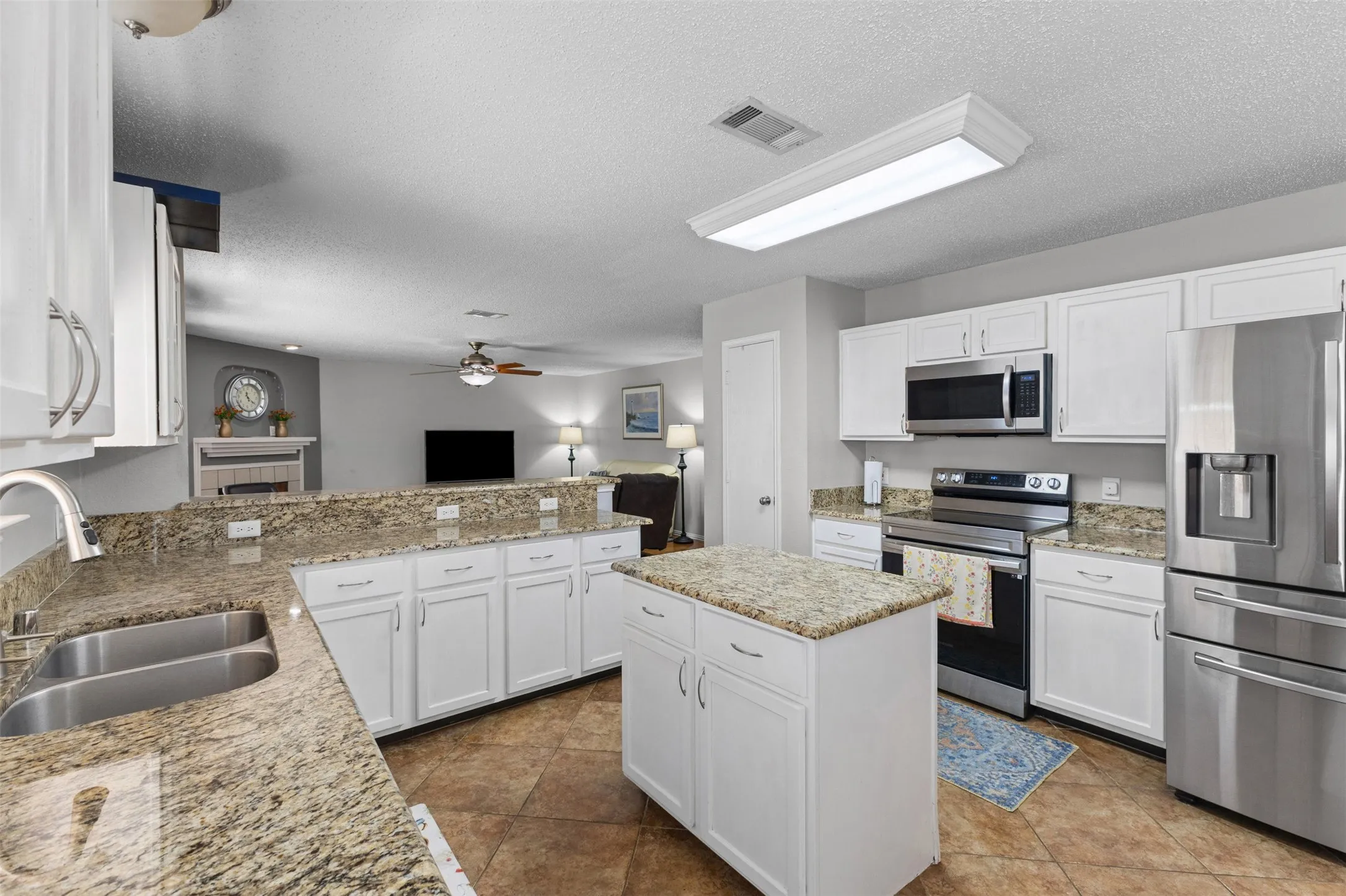Spacious kitchen featuring white cabinetry, granite countertops, stainless steel appliances, a center island, and tile flooring
