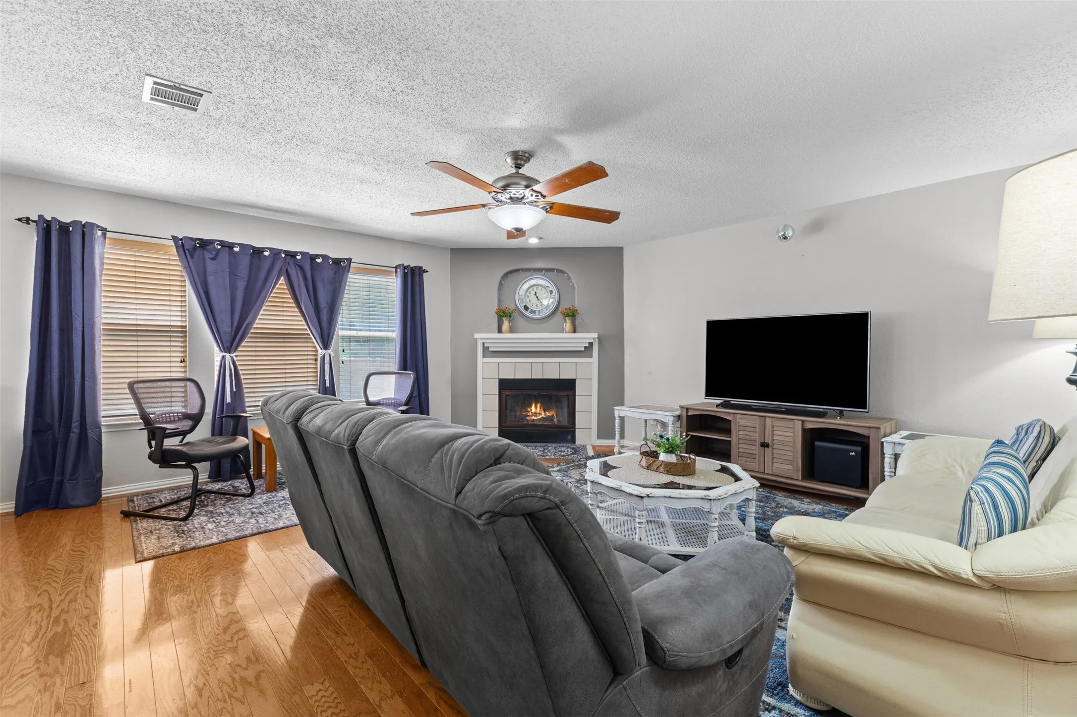 Inviting living room featuring hardwood flooring, a fireplace with a white mantel, and a ceiling fan