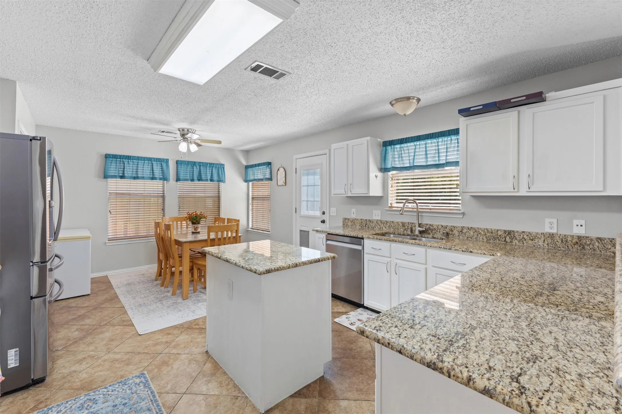Kitchen featuring white cabinetry, granite countertops, tile flooring, a central island, and a dining area with multiple windows
