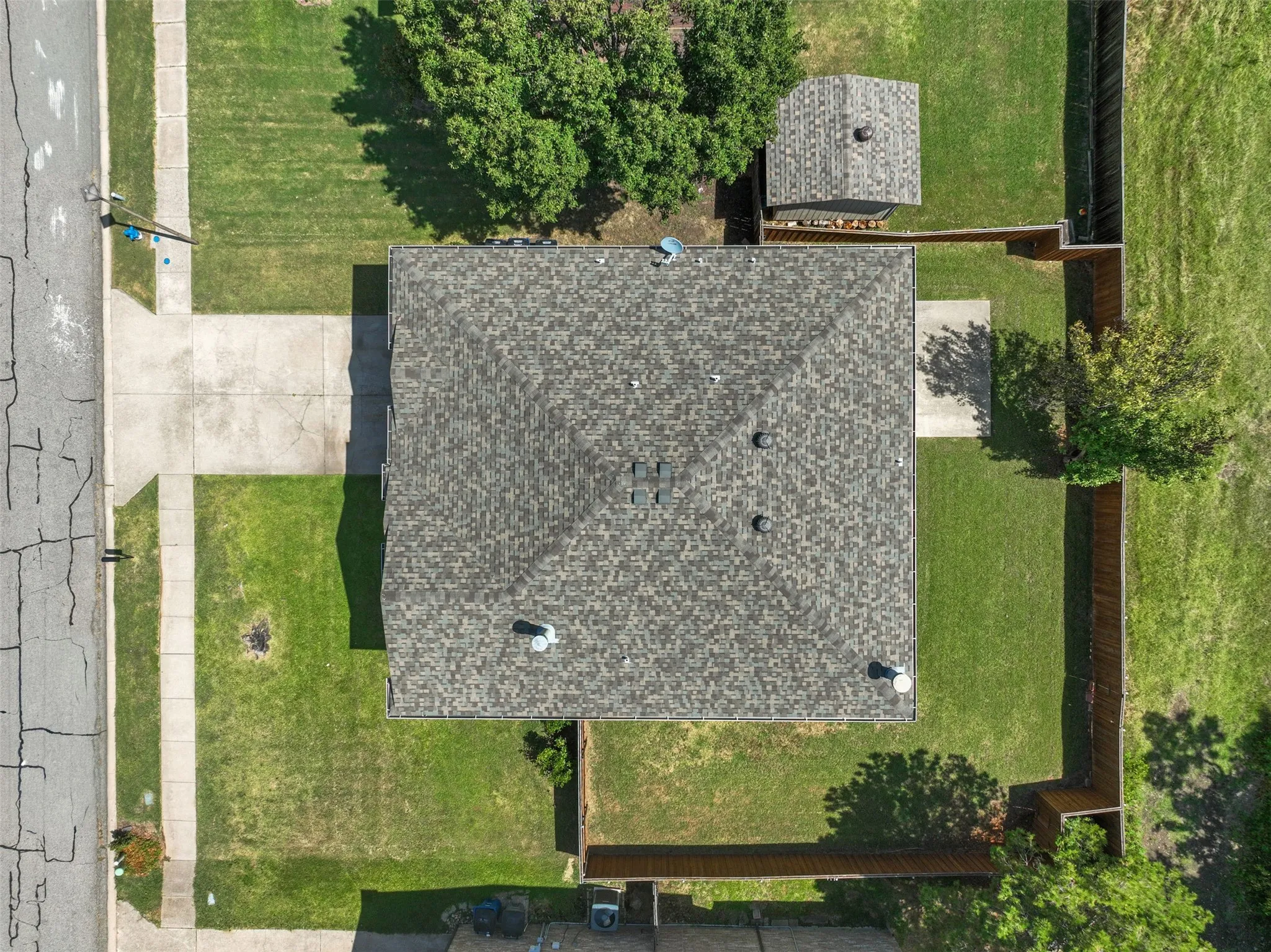 Aerial perspective showcasing a property with a shingled roof, extensive green lawn, concrete driveway, and concrete walkways