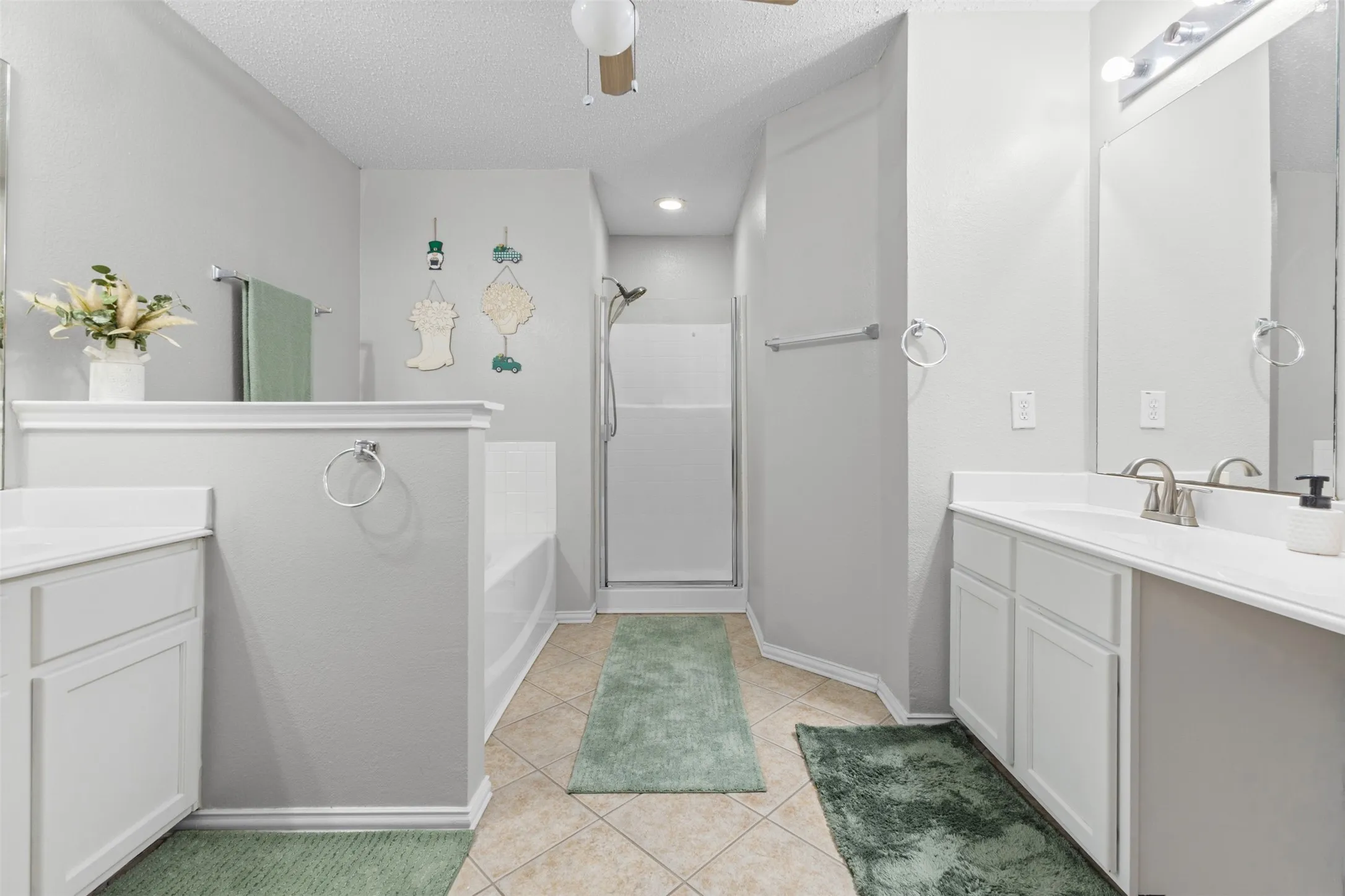 Spacious bathroom featuring dual vanities with integrated sinks, a built-in soaking tub, a separate shower enclosure, and neutral tile flooring