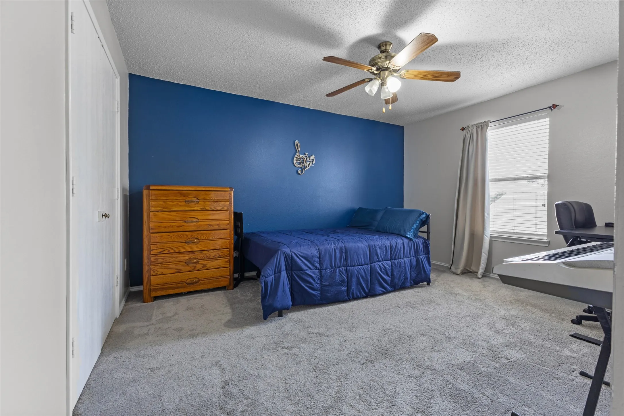 Spacious room featuring a deep blue accent wall, neutral carpeting, and a ceiling fan with integrated lighting