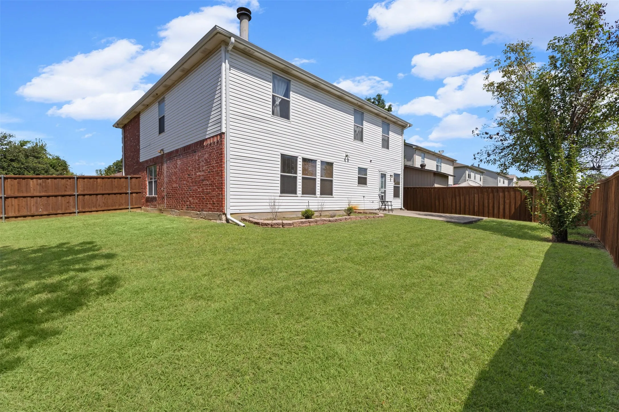 Spacious backyard featuring a lush green lawn, full privacy fencing, and a concrete patio space