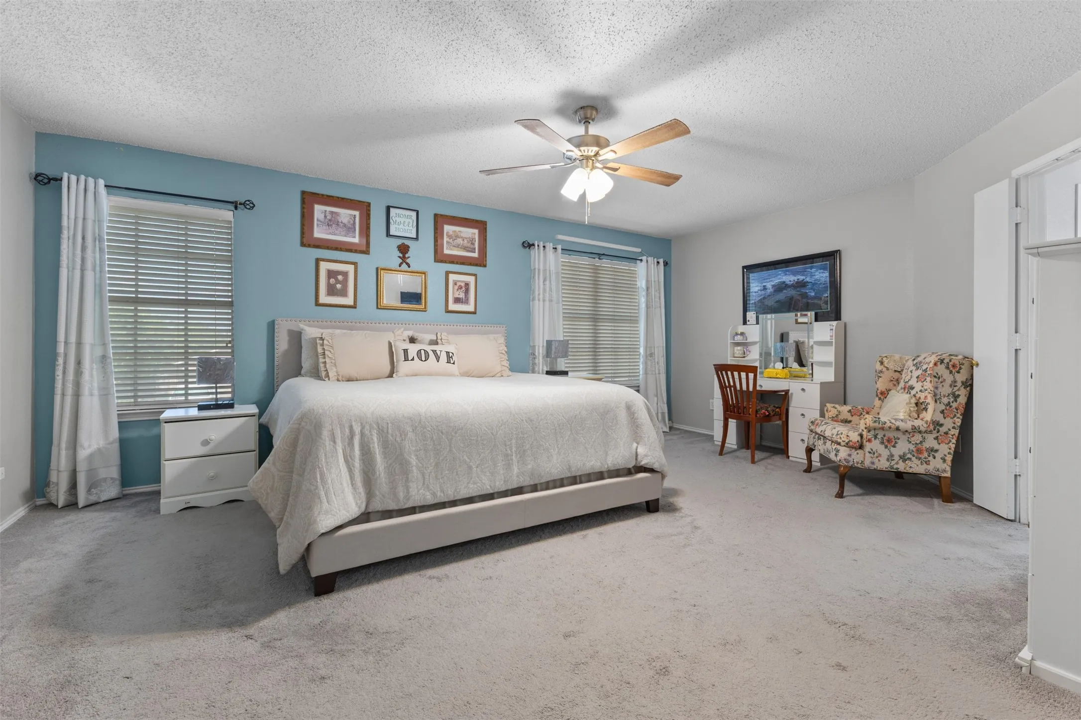 Spacious bedroom featuring light grey carpet flooring, two windows with blinds and curtains, and a ceiling fan with light fixture