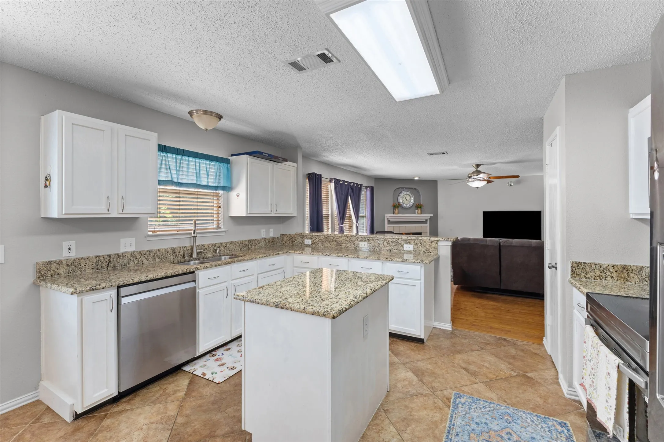 Well-appointed kitchen featuring white cabinetry, light-toned countertops, a stainless steel dishwasher, and a central island