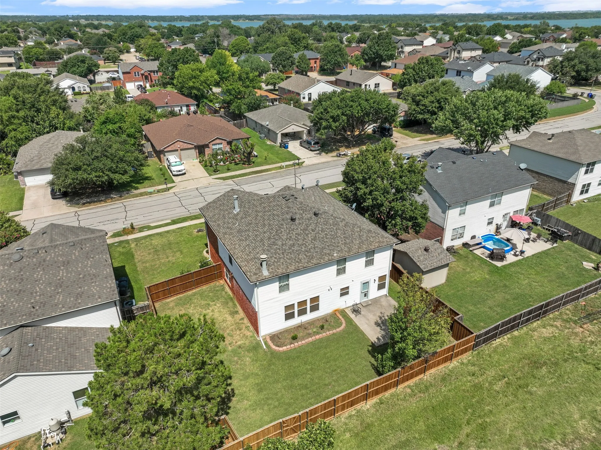 Two-story residence featuring a fenced backyard, mature trees, and a concrete patio