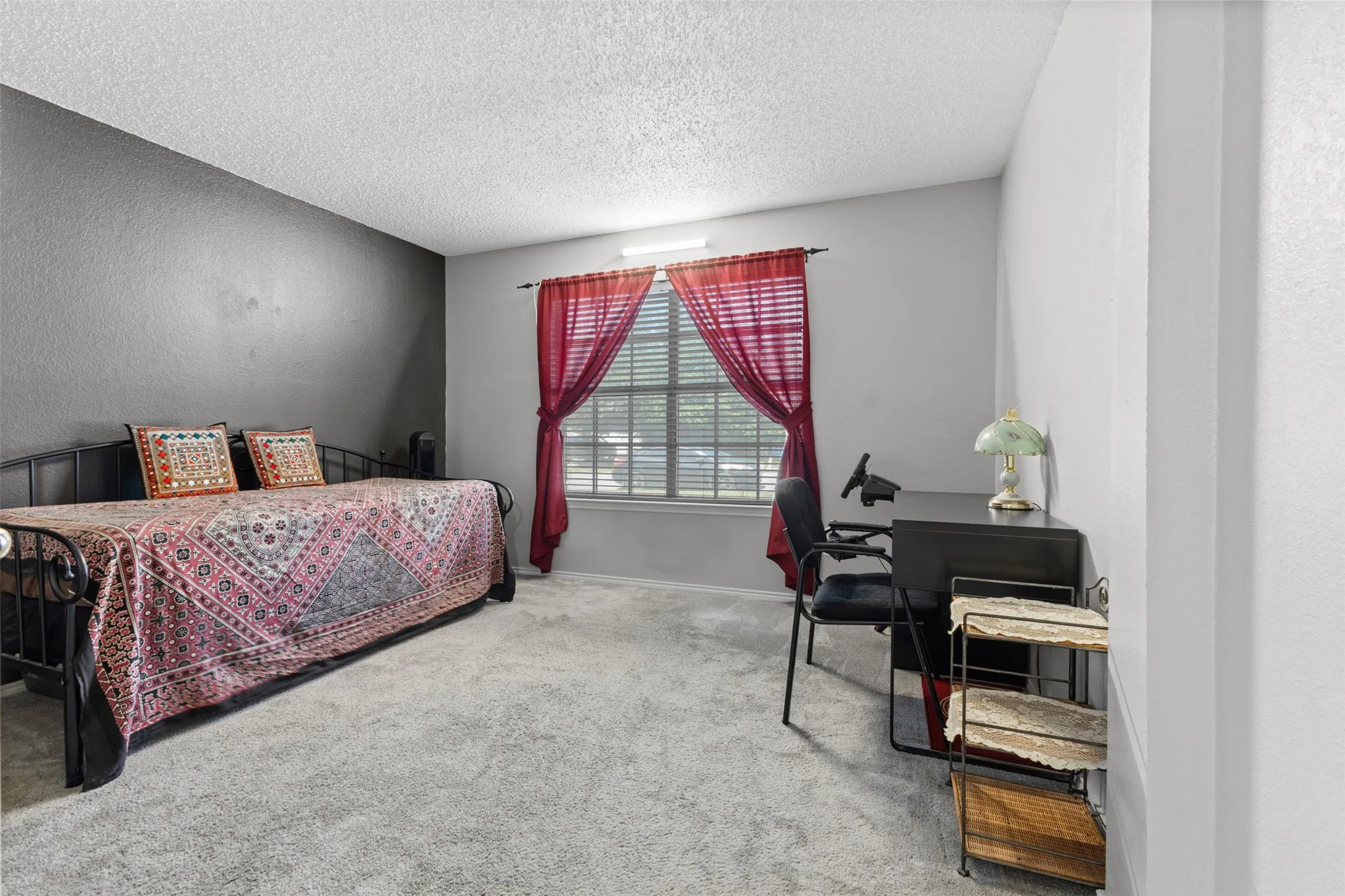 Room featuring light gray carpeting, a textured dark gray accent wall, and a window with horizontal blinds