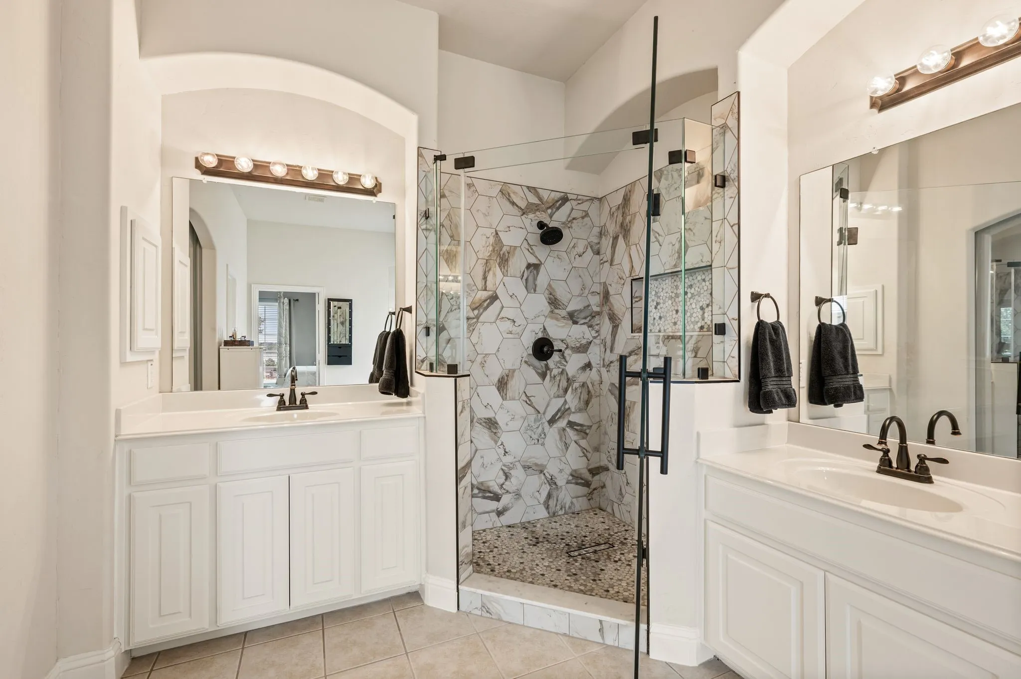 Luxurious primary bath featuring dual vanities & a stunning designer walk-in shower (2025) with custom tile, frameless glass, recessed shampoo box and custom floor drain!
