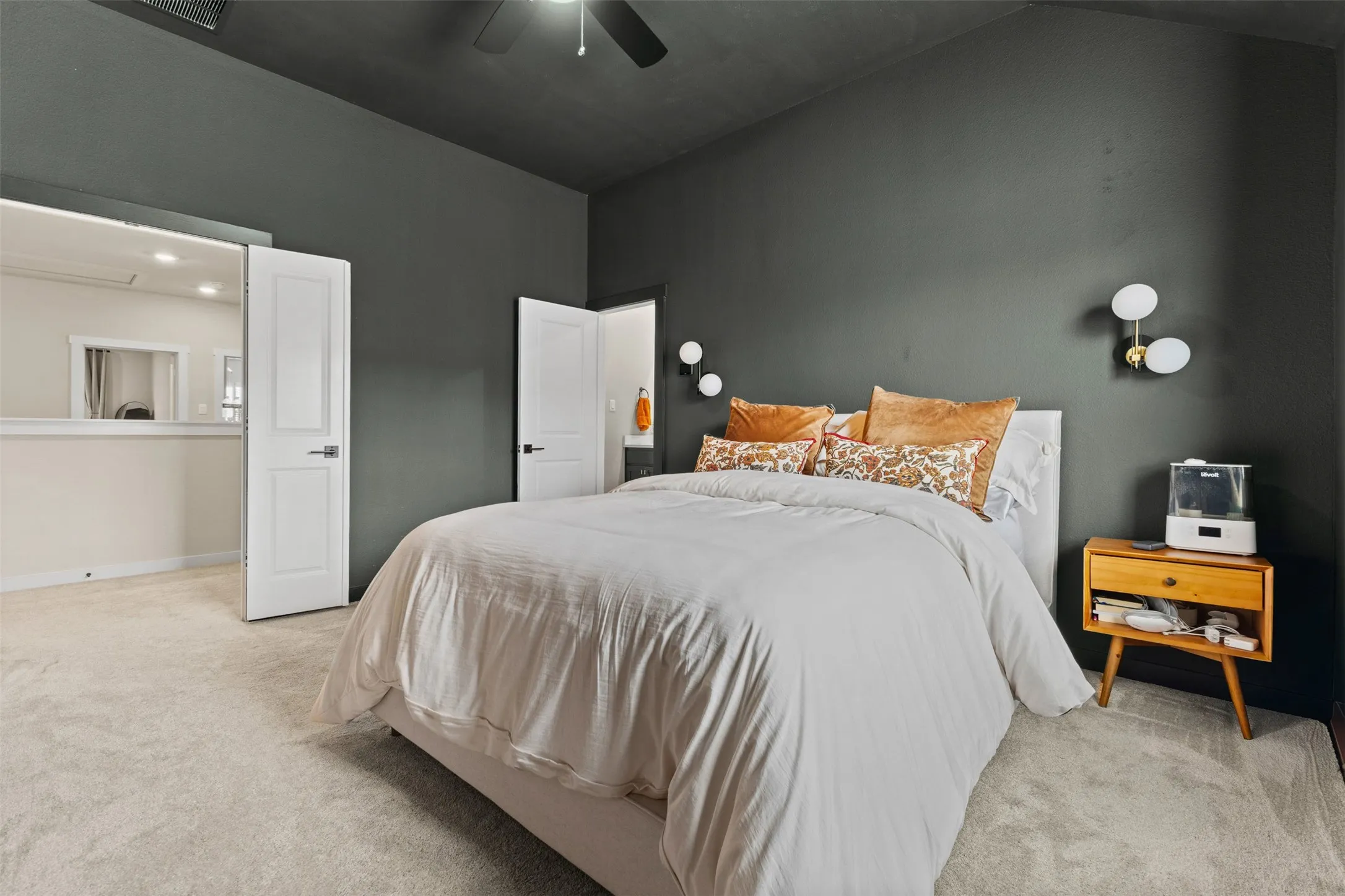 Vaulted ceiling bedroom featuring dark accent walls, light-toned carpeting, white panel doors, and modern wall sconces
