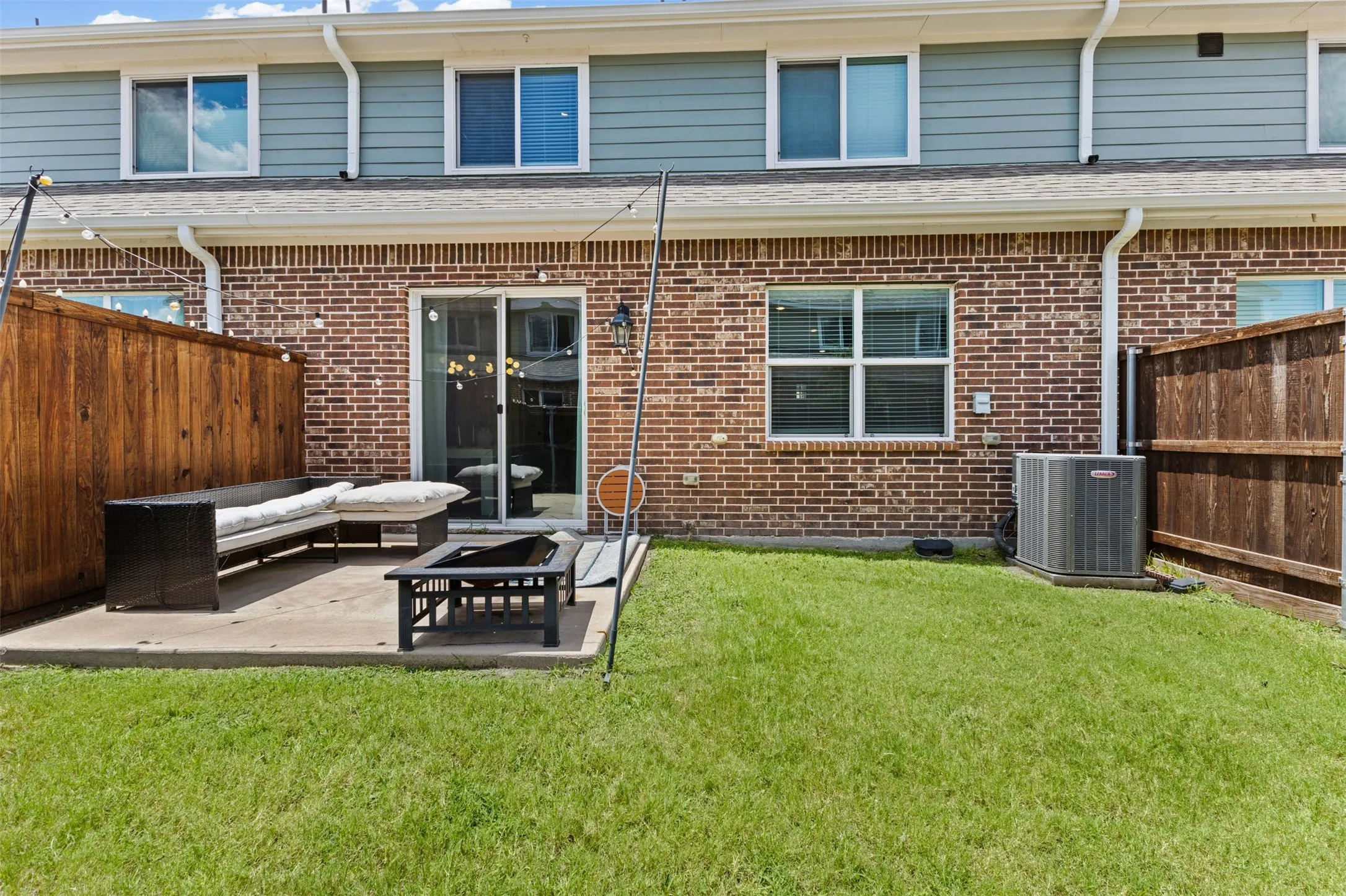 Private patio with concrete slab and turf lawn, featuring brick and siding exterior and privacy fencing