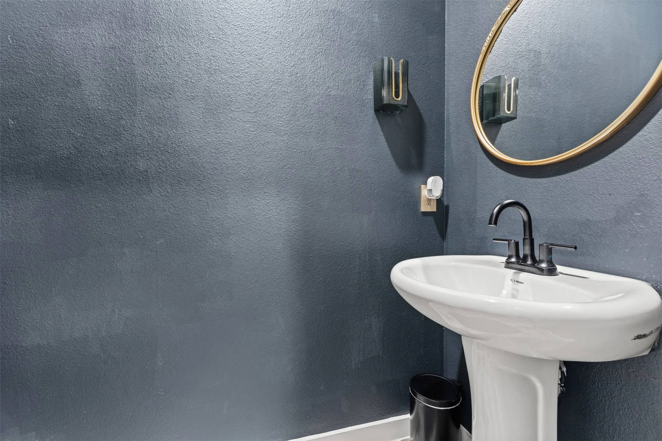 Pedestal sink with dark-toned fixtures and a coordinating oval mirror