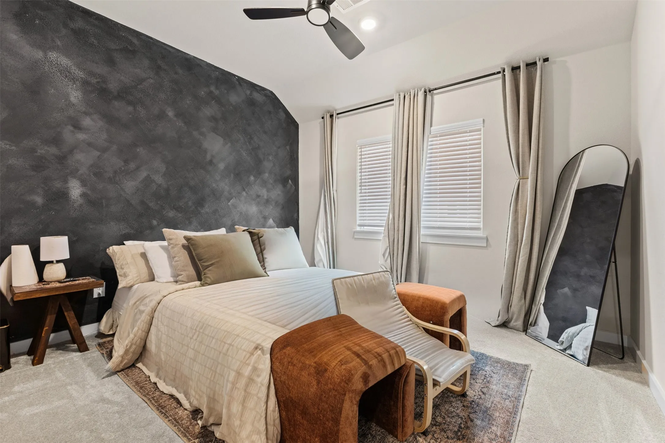 Bedroom featuring a textured accent wall, light-colored carpeting, two windows with blinds and drapes, and a ceiling fan