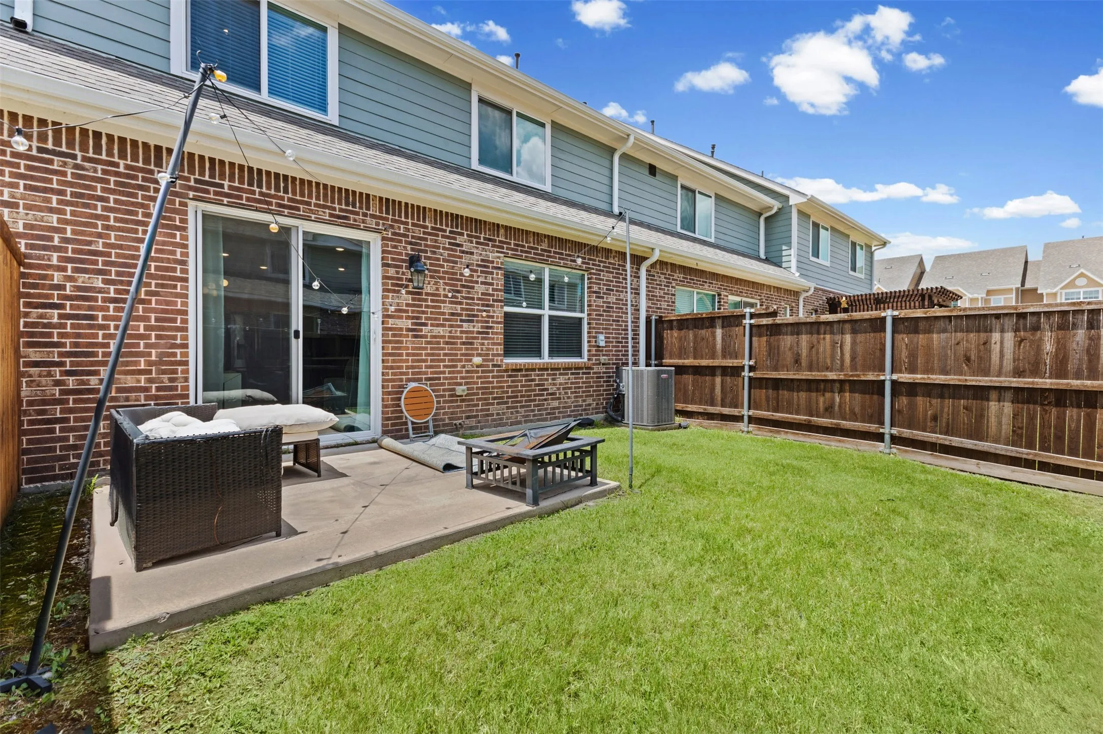 Private backyard space featuring a concrete patio, sliding glass doors, brick exterior, and wood fencing