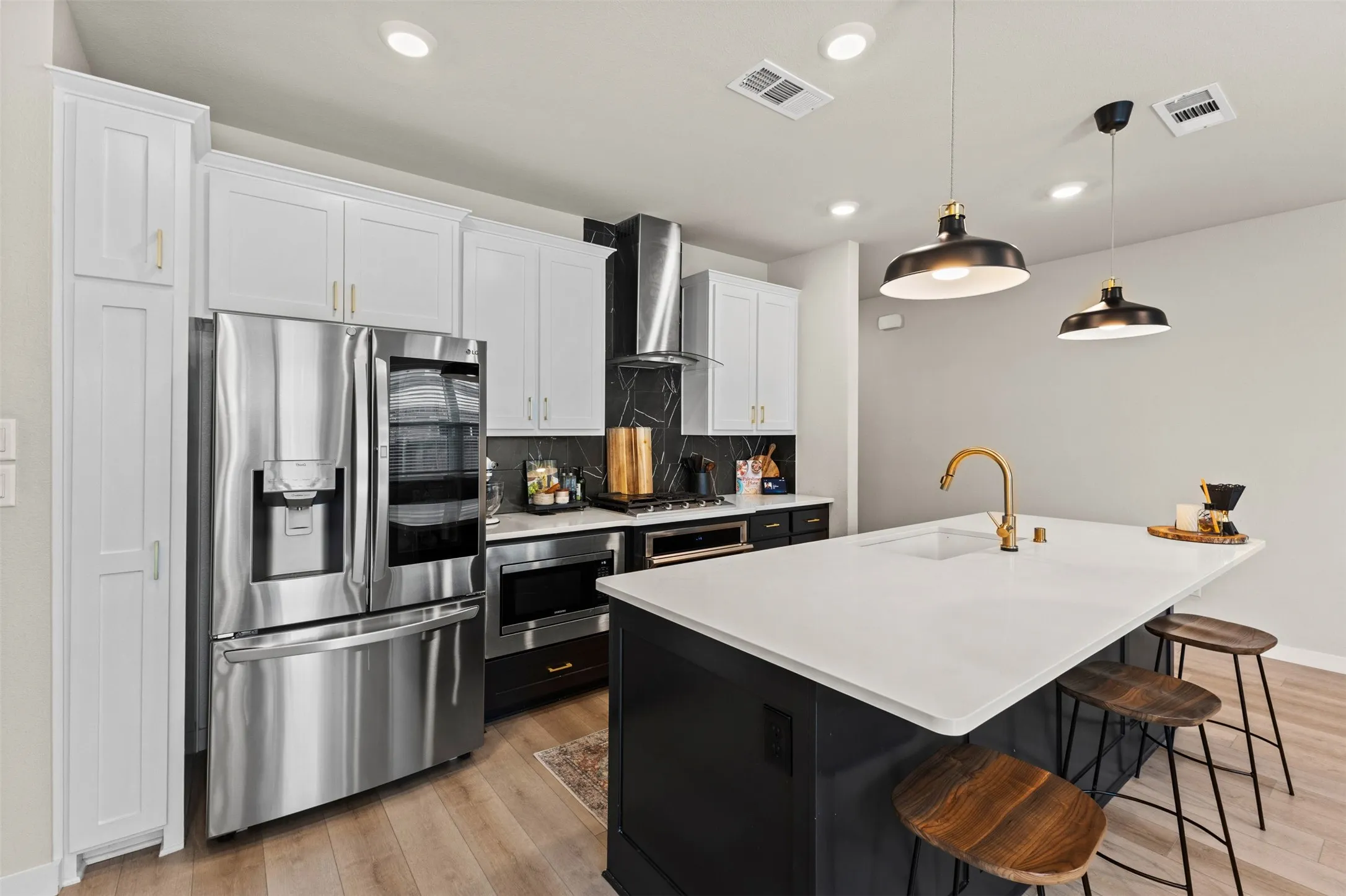 Modern kitchen featuring a large island with a white countertop and seating for three, stainless steel appliances, and wood-finish flooring