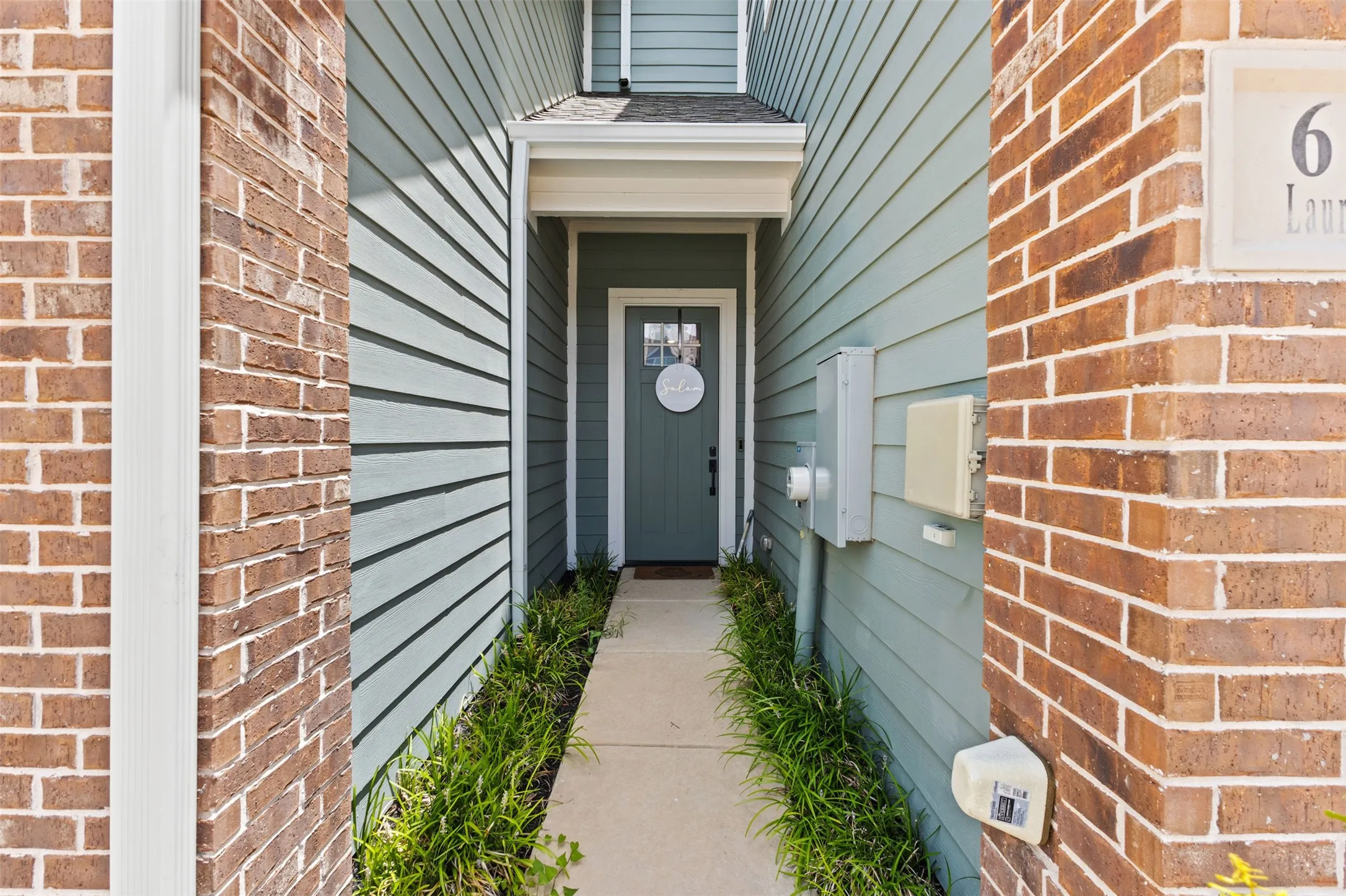 Inviting entry featuring a solid paneled door with upper glass paneling, flanked by a concrete pathway and established perimeter landscaping