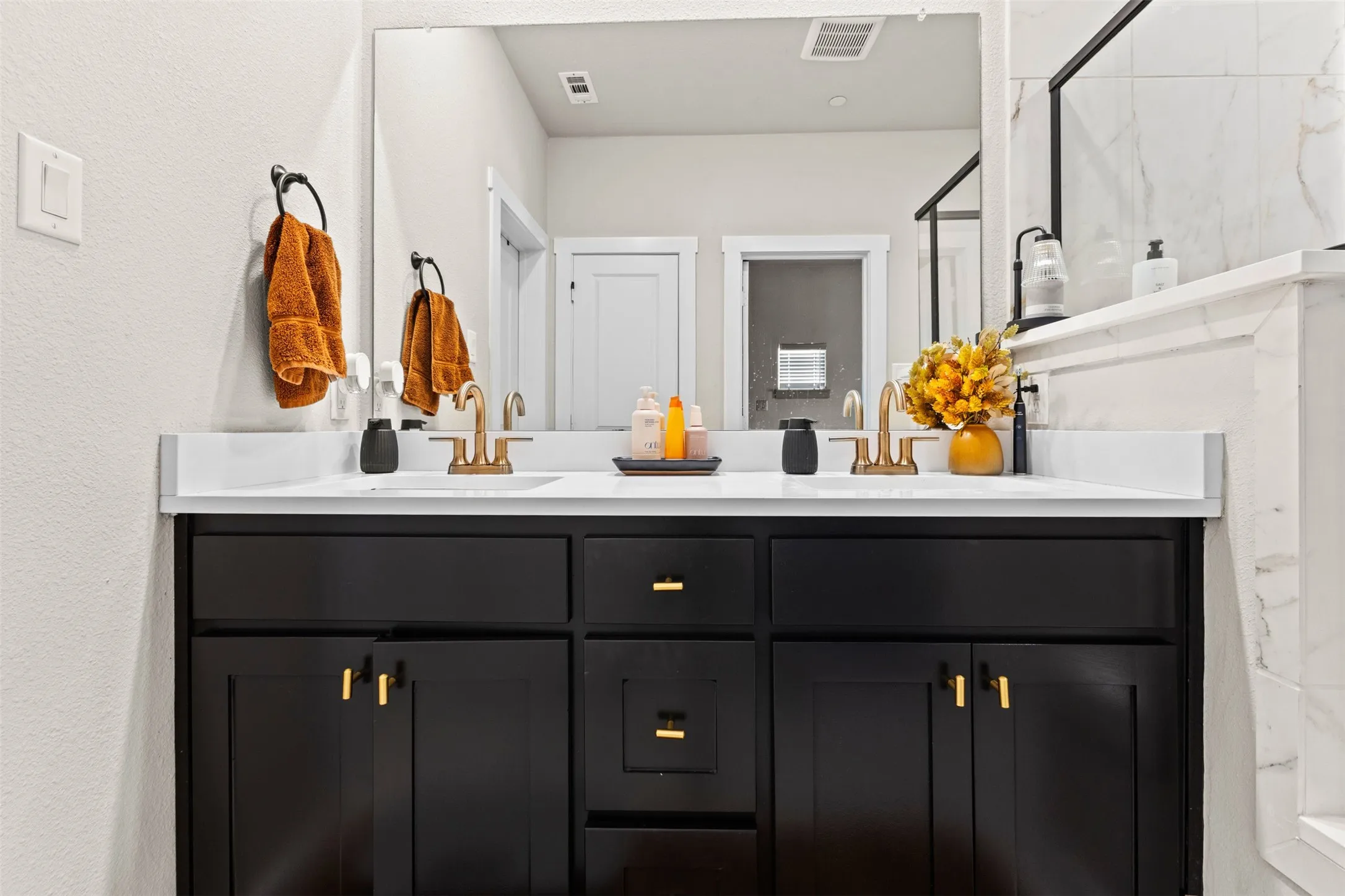Dual vanity featuring black shaker-style cabinetry, white countertops, and gold-finish fixtures