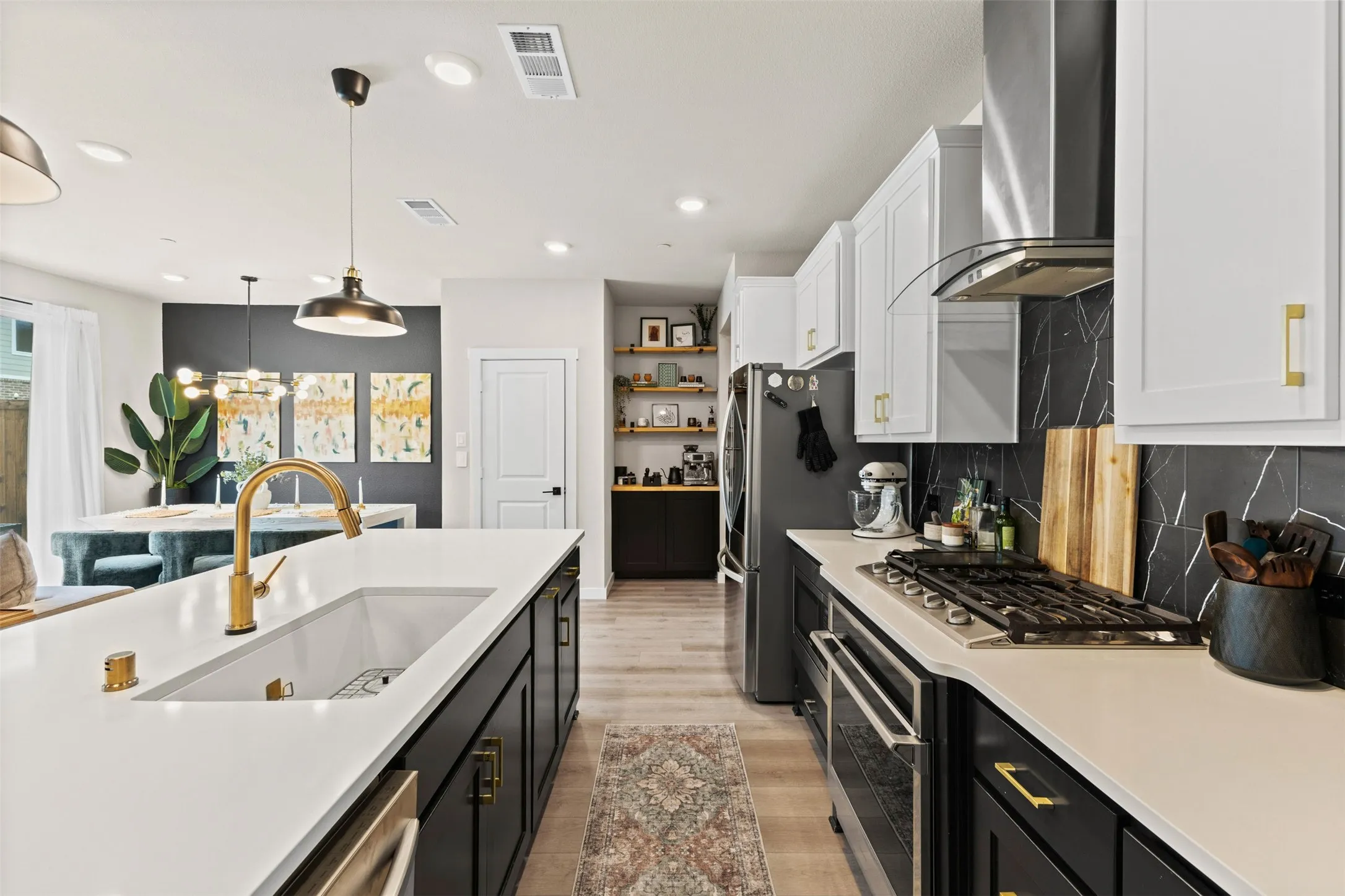 Open-concept kitchen featuring a white farmhouse sink, gold-finish faucet, white countertops, and black cabinetry