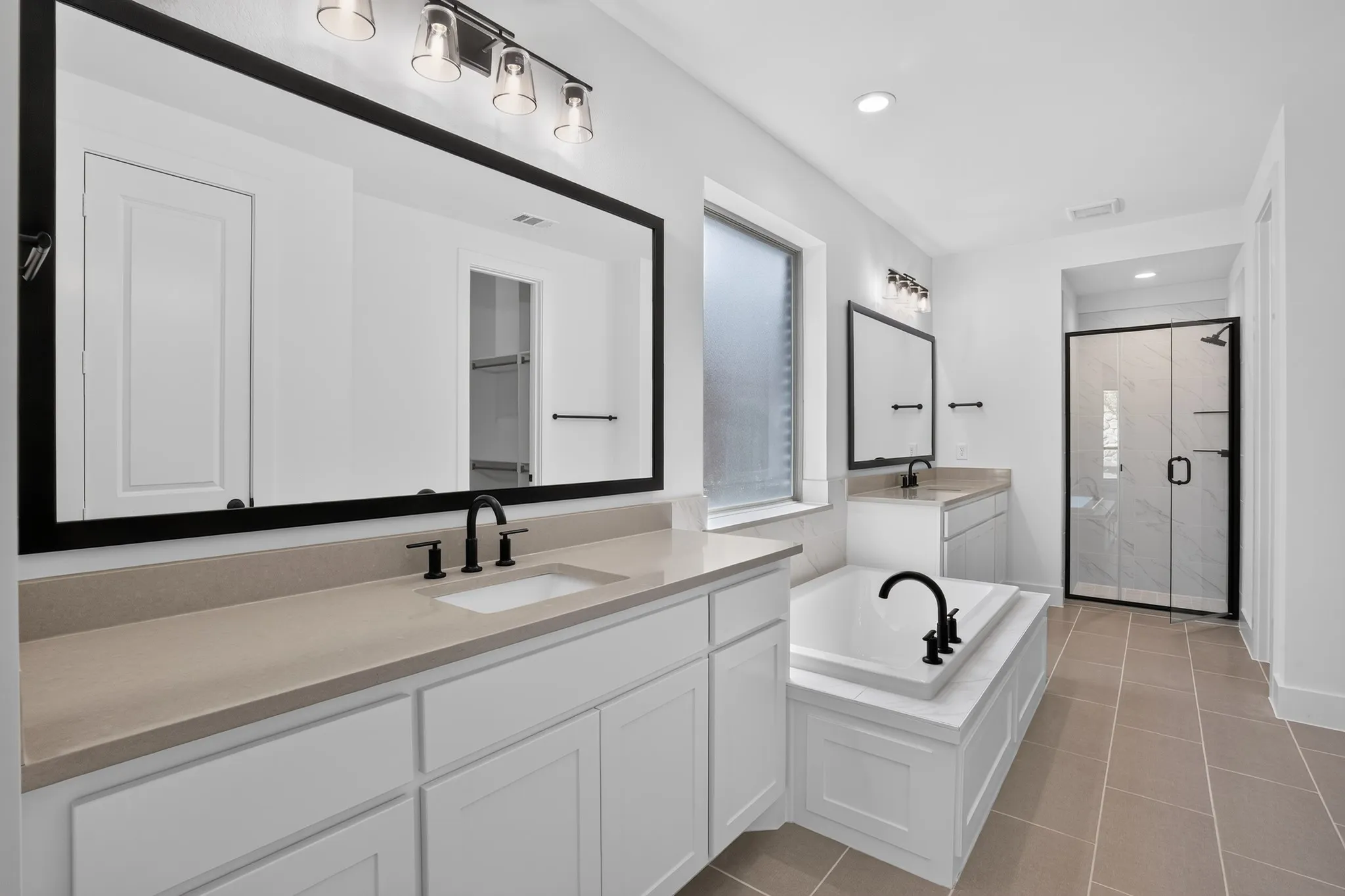Dual vanity with stone countertops, white shaker cabinetry, large format tile flooring, built-in bathtub, and a frameless glass shower enclosure