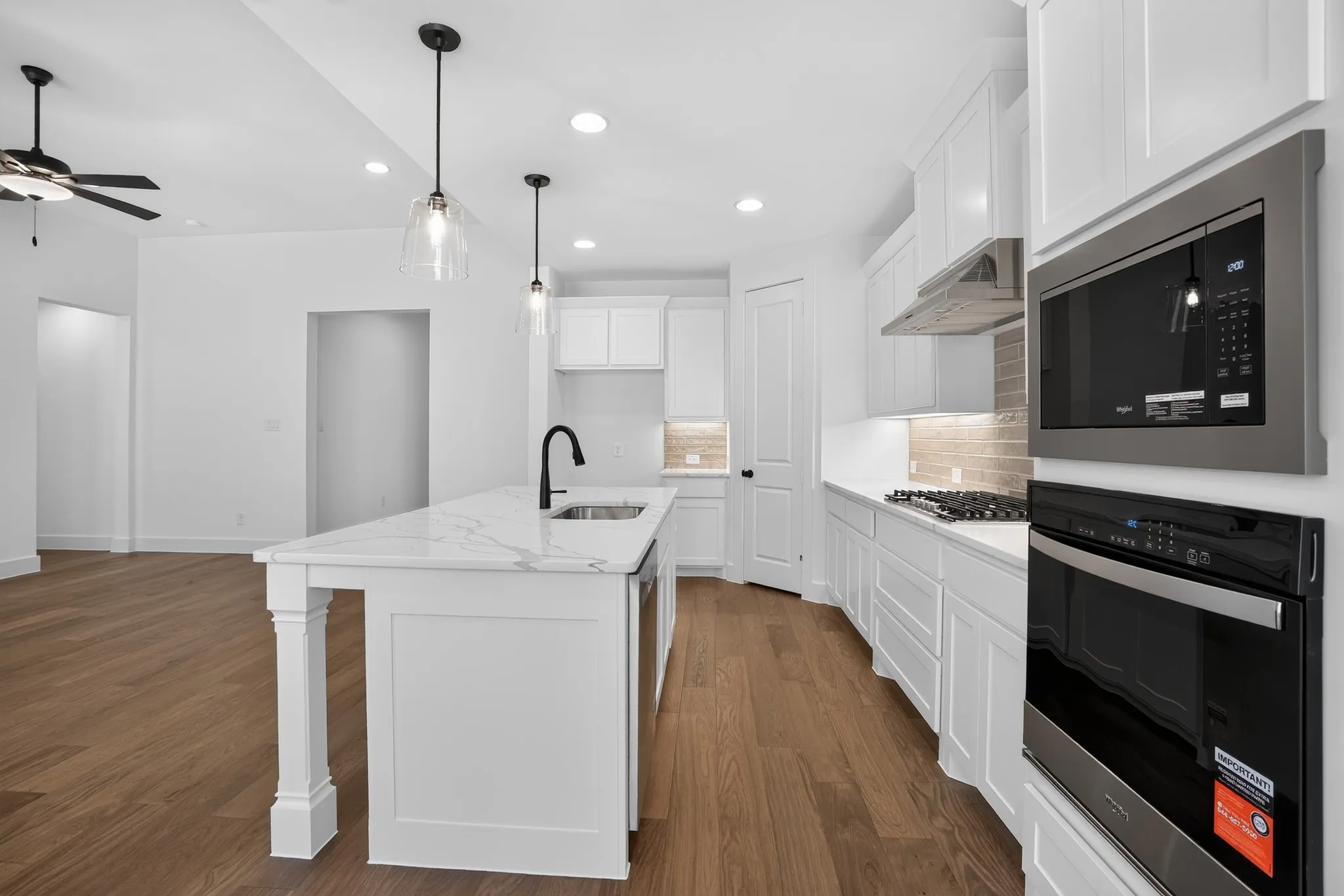 White shaker cabinetry with dark hardware, a center island with a sink and a gooseneck faucet, light-toned wood-finish flooring, recessed lighting, and stainless steel built-in appliances