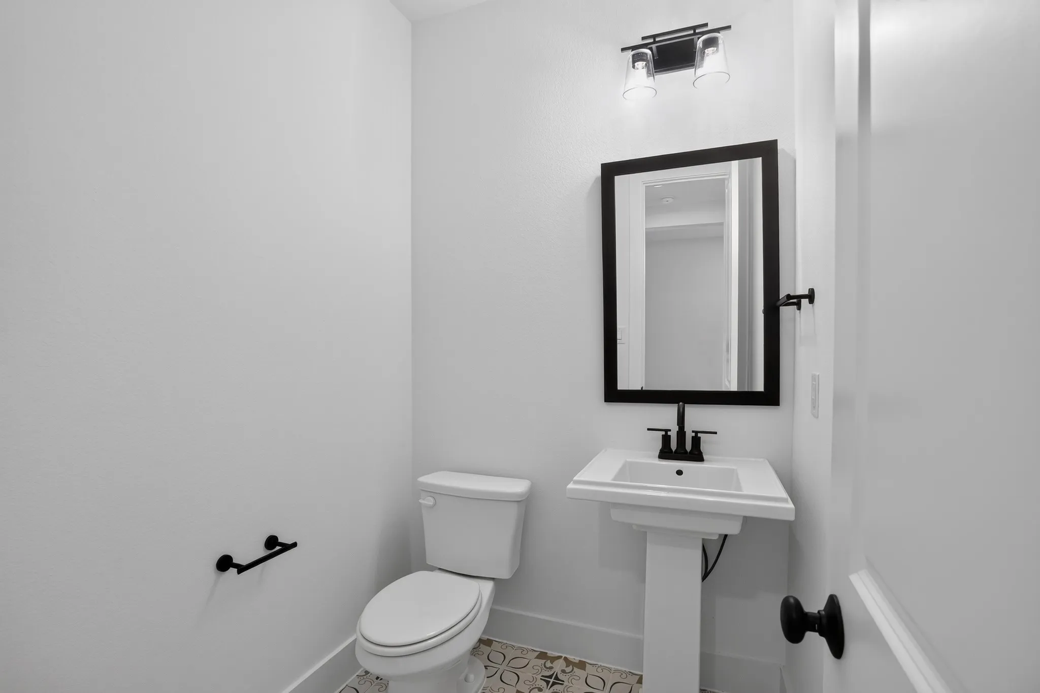 Pedestal sink with a two-handle faucet, rectangular framed mirror, and decorative tile flooring