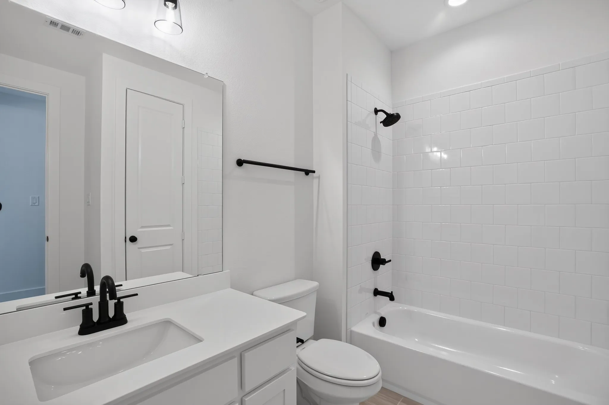 White subway tile shower surround, matte black bath fixtures, white vanity with integrated sink, matte black faucet, and white toilet